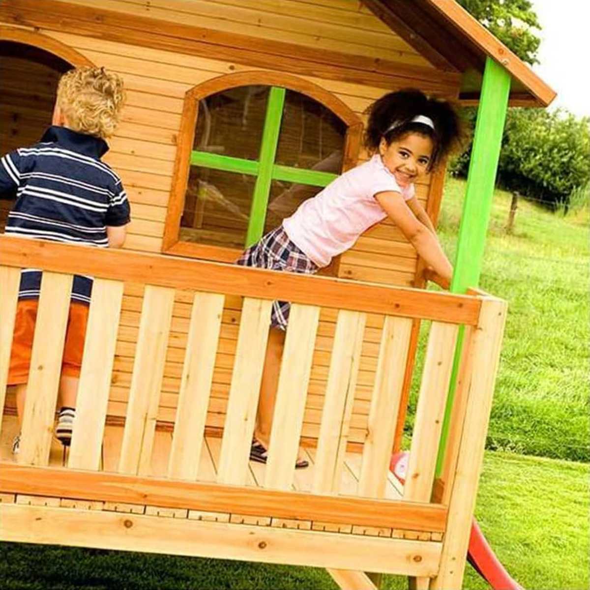 Zwei Kinder spielen auf einem Holzspielhaus. Ein Kind klettert, das andere schaut von hinten zu.