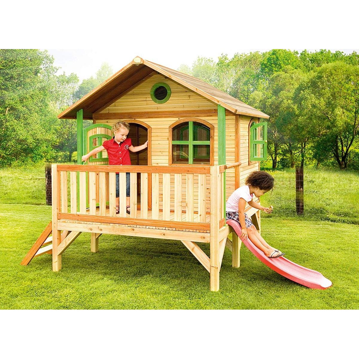 Kinder spielen auf einem Holzspielhaus mit Rutsche. Grünes Gras und Bäume sind im Hintergrund.