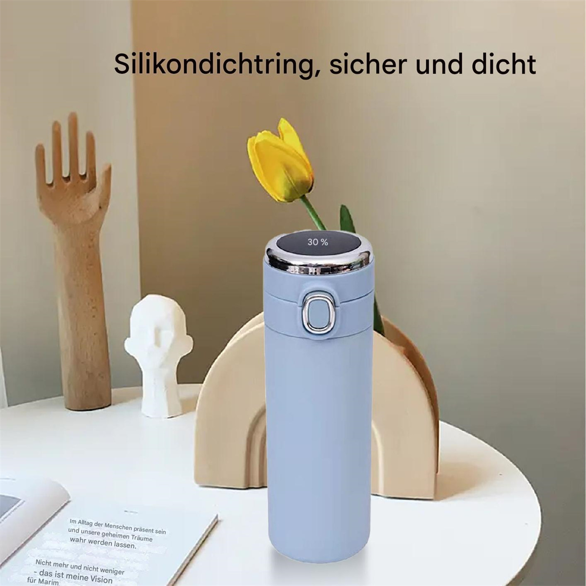 Blaue Wasserflasche mit silberner Kappe und gelber Blume auf weißem Tisch.