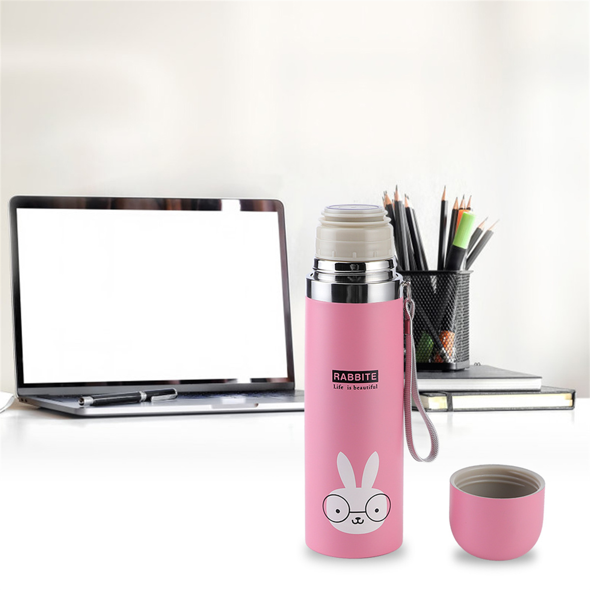 Rosa Thermoskanne mit Hasen-Design. Sie hat einen kleinen Griff und ist offen, mit einem Deckel daneben, auf einem Schreibtisch mit Laptop.