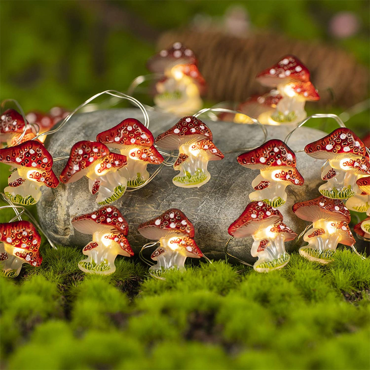 Lichterkette mit pilzförmigen Lichtern. Sie sind rot mit weißen Punkten und liegen auf Moos und Stein.