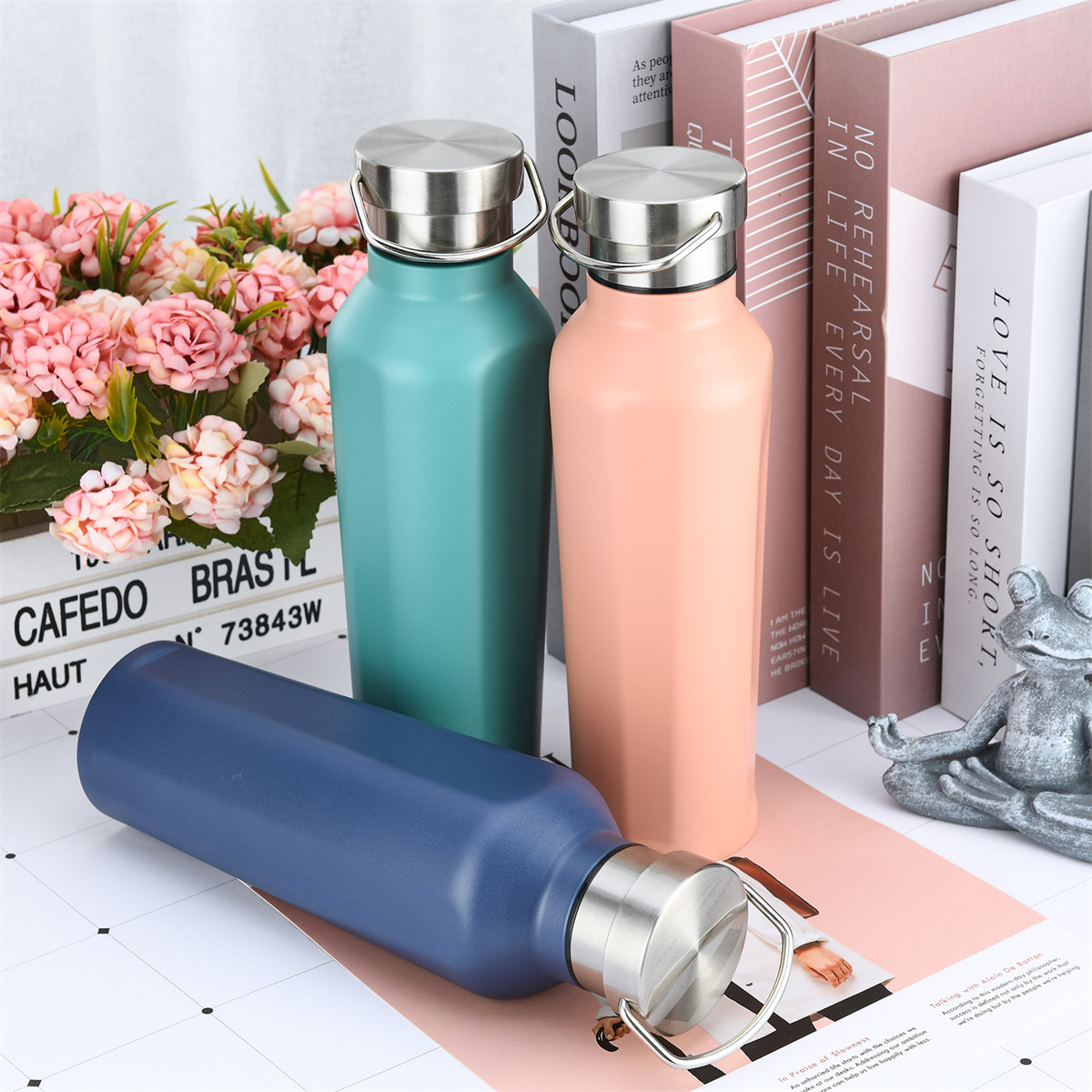 Drei isolierte Wasserflaschen in verschiedenen Farben. Rosa, Blau und Türkis. Bücher und Blumen im Hintergrund.