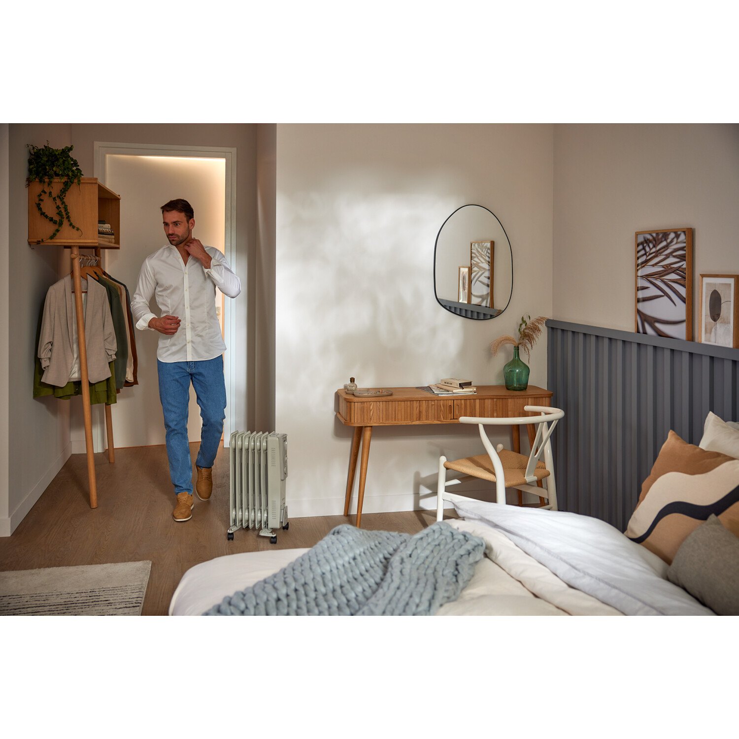 Een man in een wit overhemd loopt een kamer binnen. Er is een bureau, bed en kachel. Neutrale kleuren.