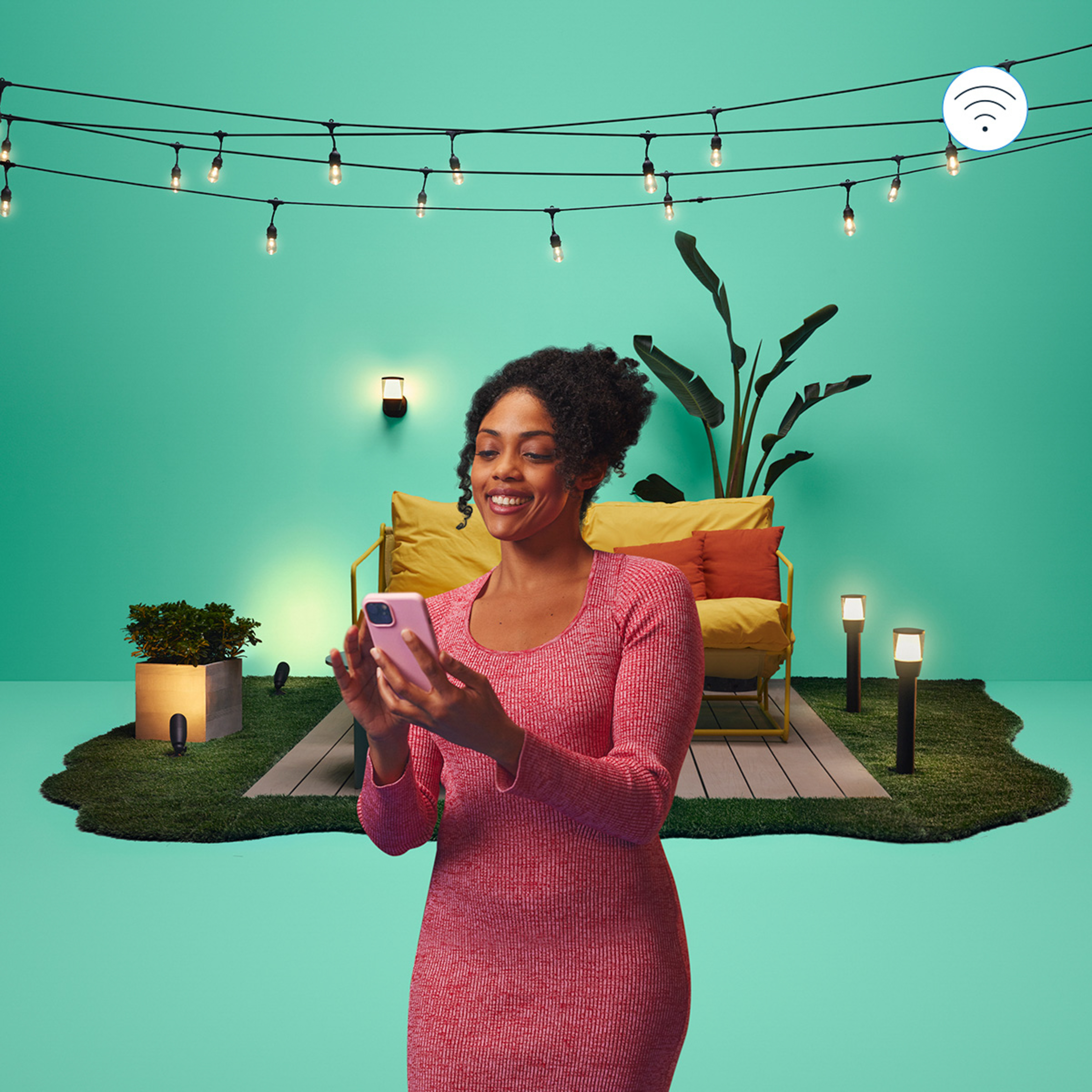 A woman using a pink phone in a backyard with lights and a green background.