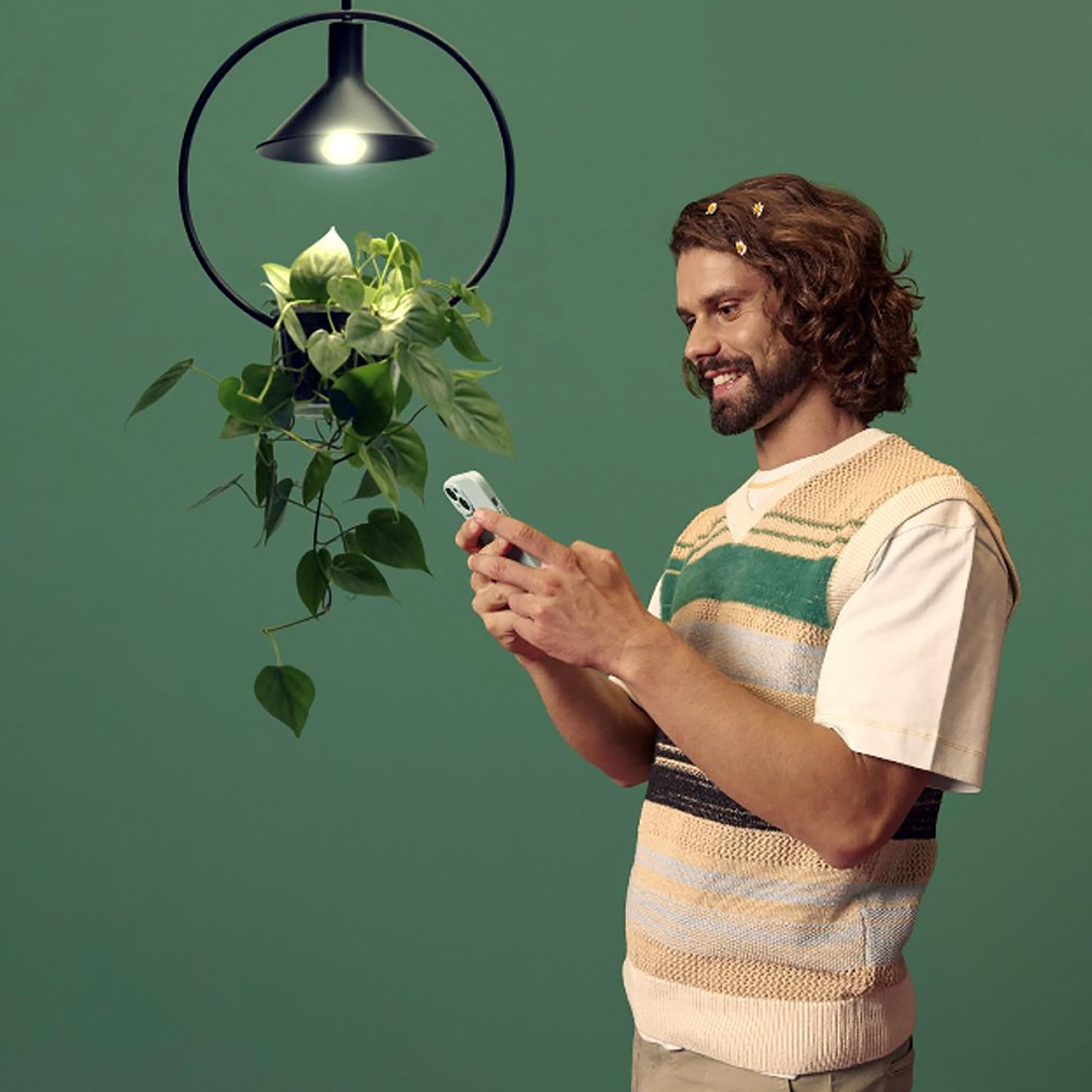 Mężczyzna patrzący na telefon, stojący blisko rośliny pod czarną lampą.
