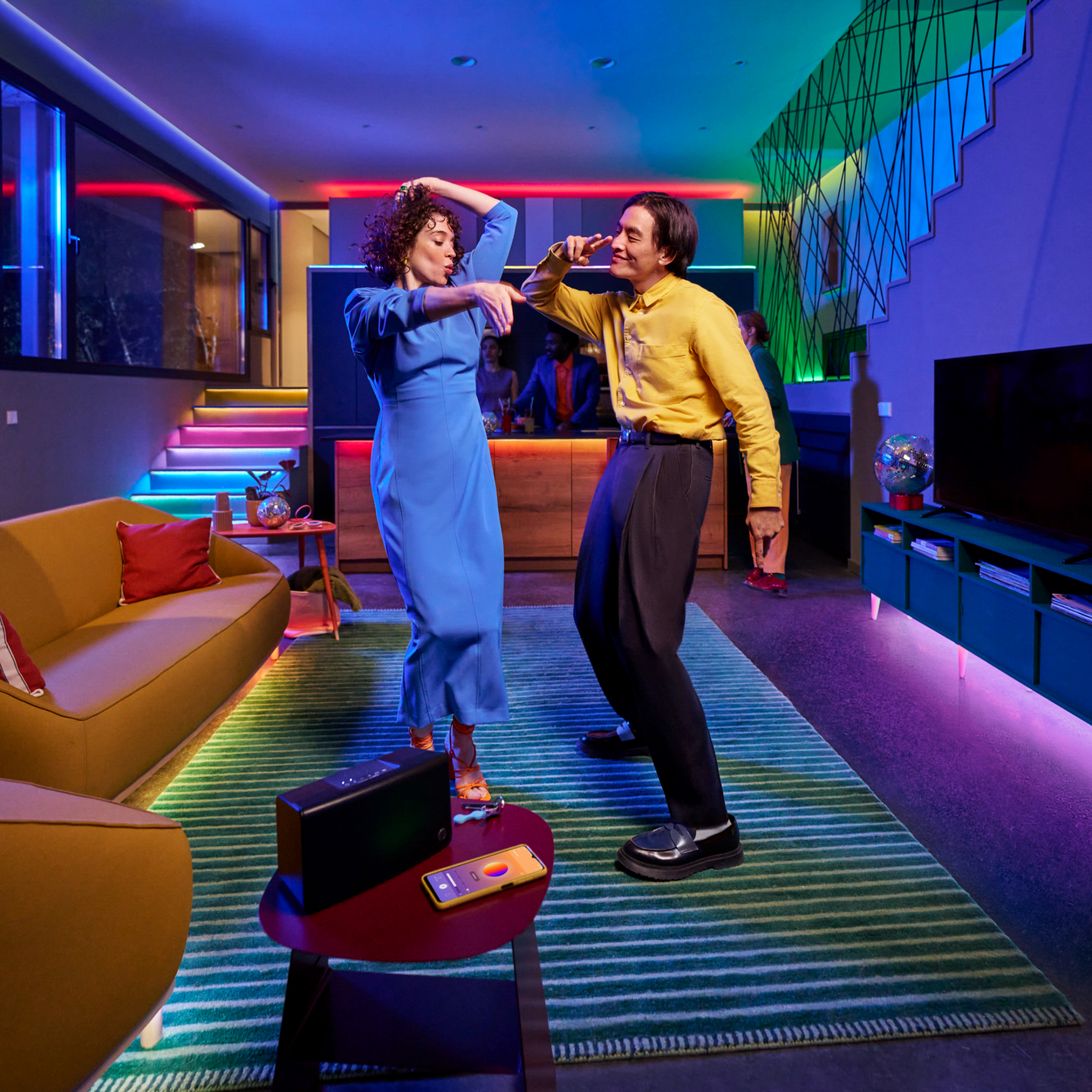 Twee mensen dansen. Een vrouw in blauw en een man in geel. Kleurrijke lichten verlichten de kamer.