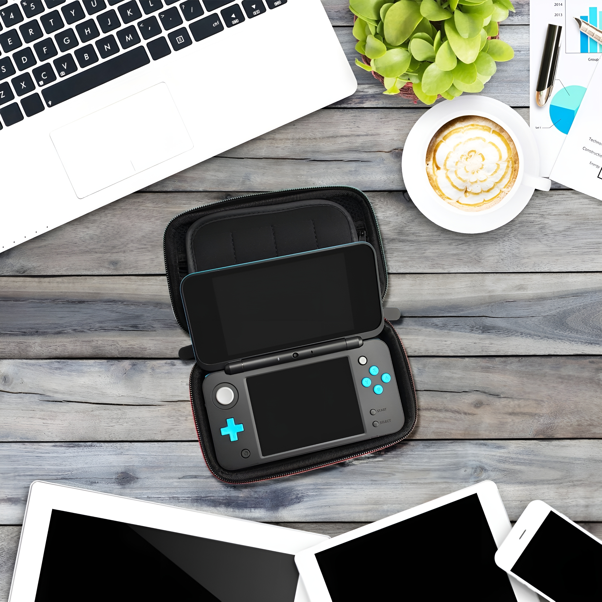 Eine Spielkonsole in einem Etui liegt auf einem Holztisch mit Laptop und Kaffee.