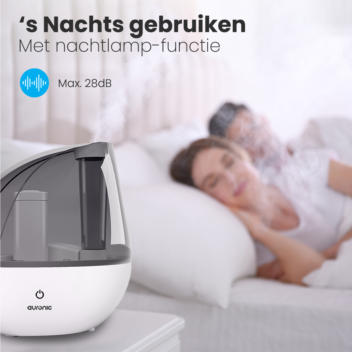 Ein schlafendes Paar mit einem Luftbefeuchter im Vordergrund. Der Luftbefeuchter ist weiß und schwarz und gibt Dampf ab.