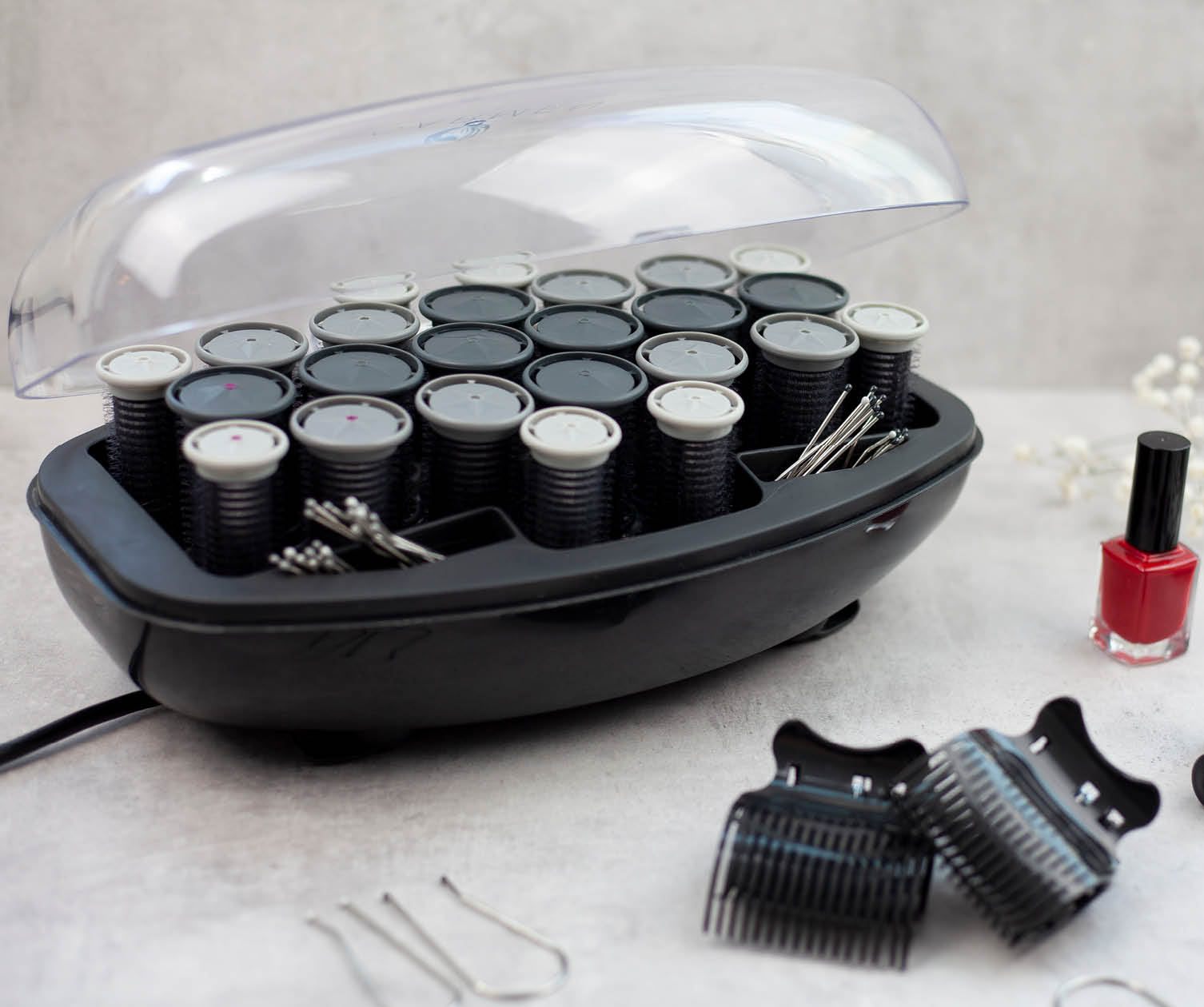 Black hair rollers in a case, with pins, clips, and a nail polish bottle, on a white surface.