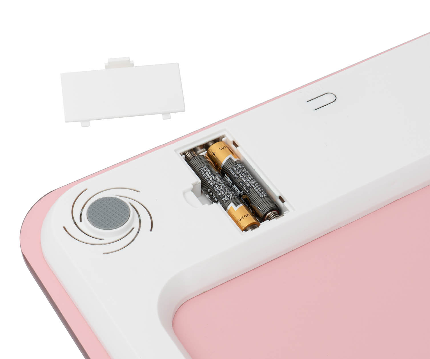 Close-up van het batterijcompartiment van een weegschaal, met twee batterijen. Een witte afdekking ligt ernaast.