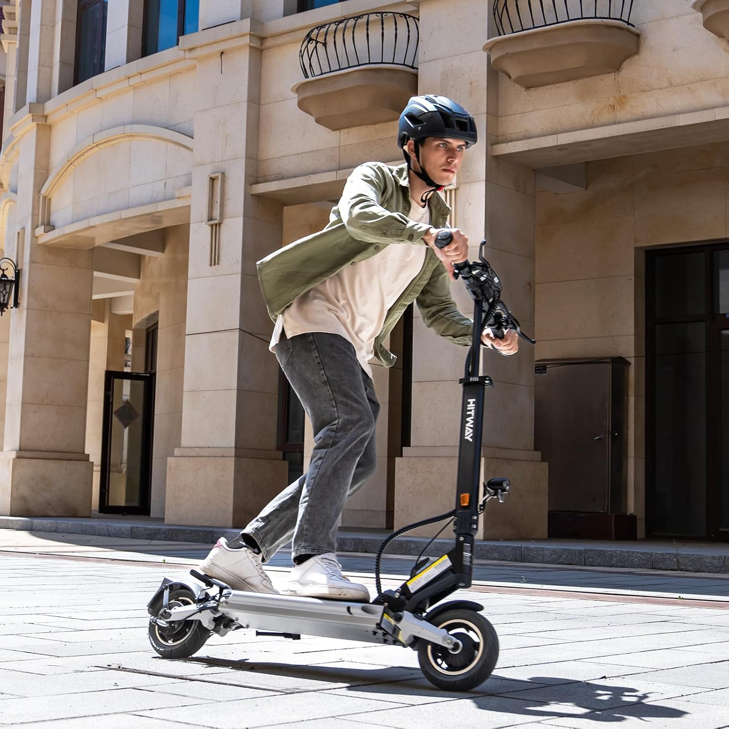 A person riding a Hitway electric scooter. The scooter is black and silver. The person wears a helmet.