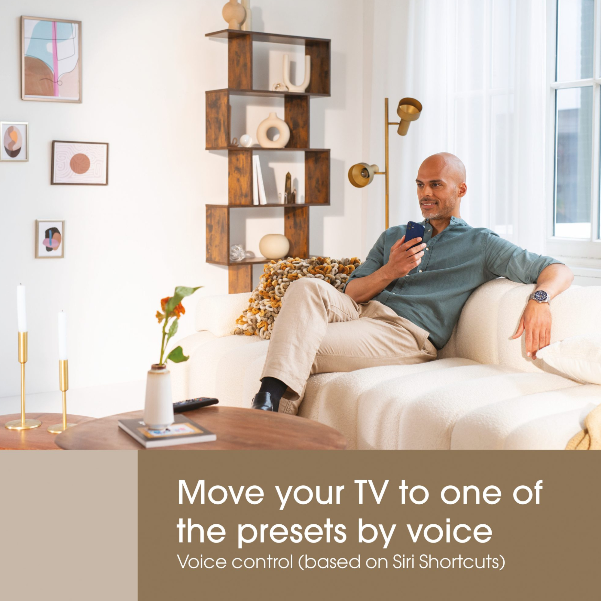 Mężczyzna siedzi na kanapie, trzymając telefon. Jest stół ze świecami i wazon z kwiatami.