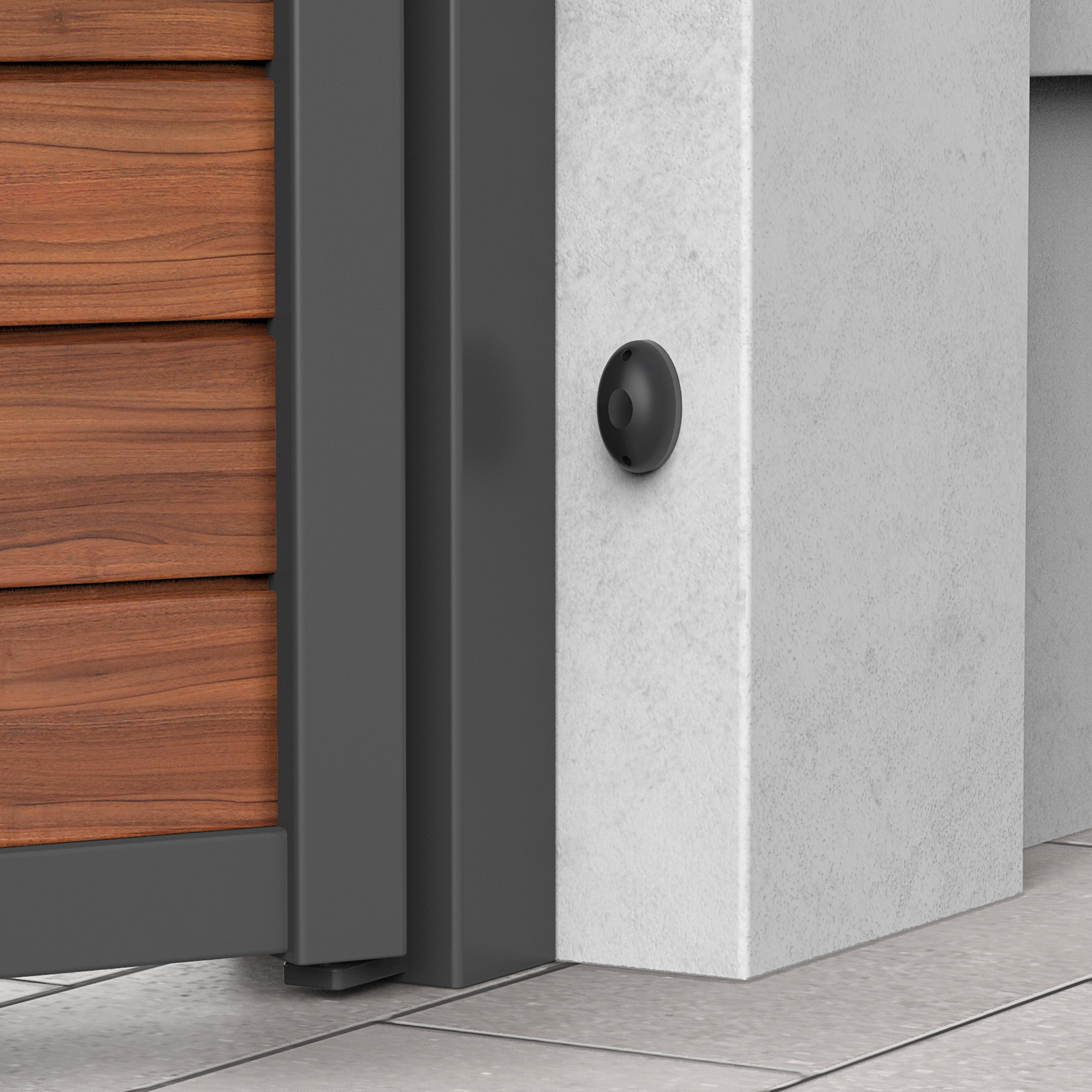 Sensore grigio scuro montato su un muro di cemento bianco accanto a un cancello di legno.