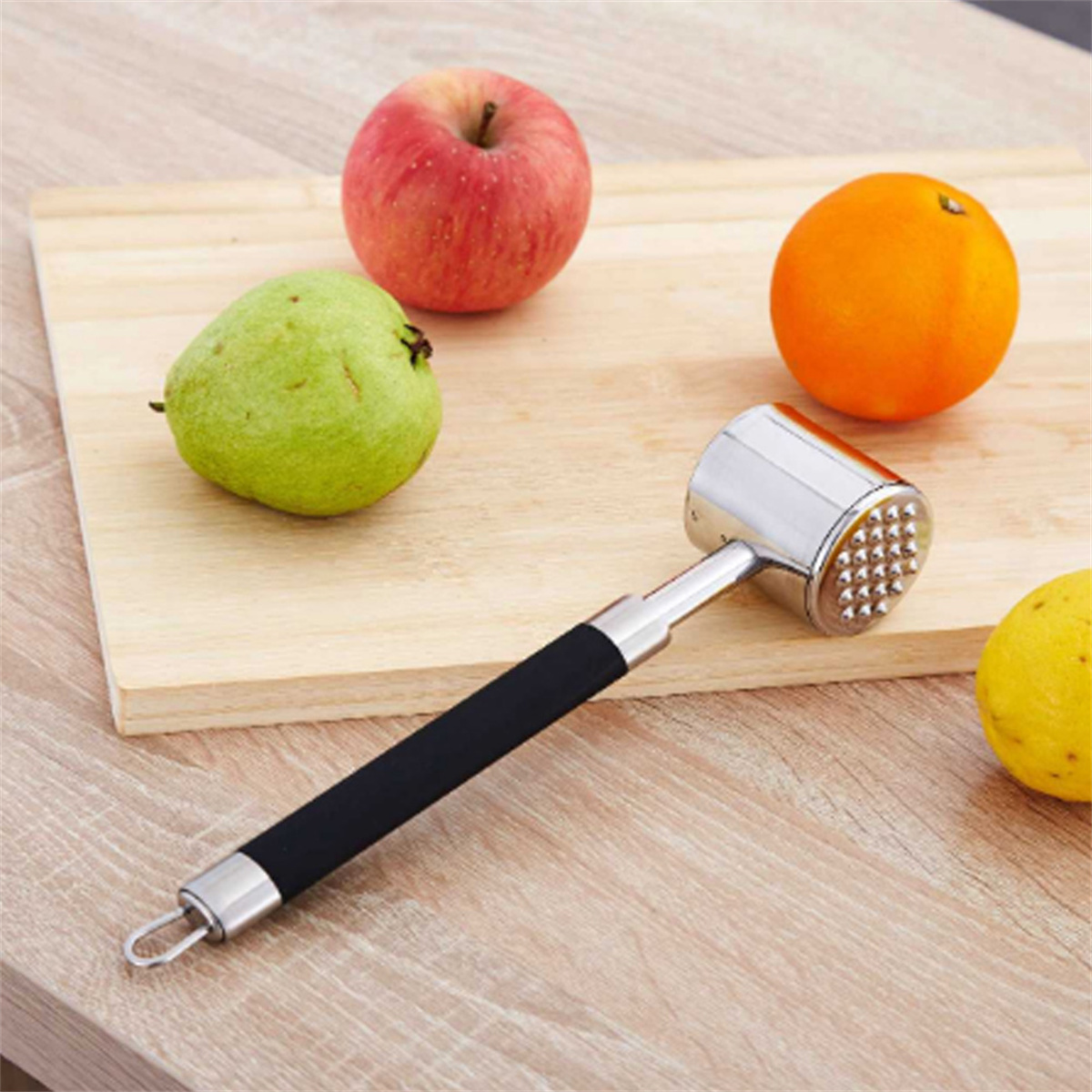 Verschiedene Früchte und ein Fleischklopfer auf einem Holzbrett. Der Tenderizer ist silber.