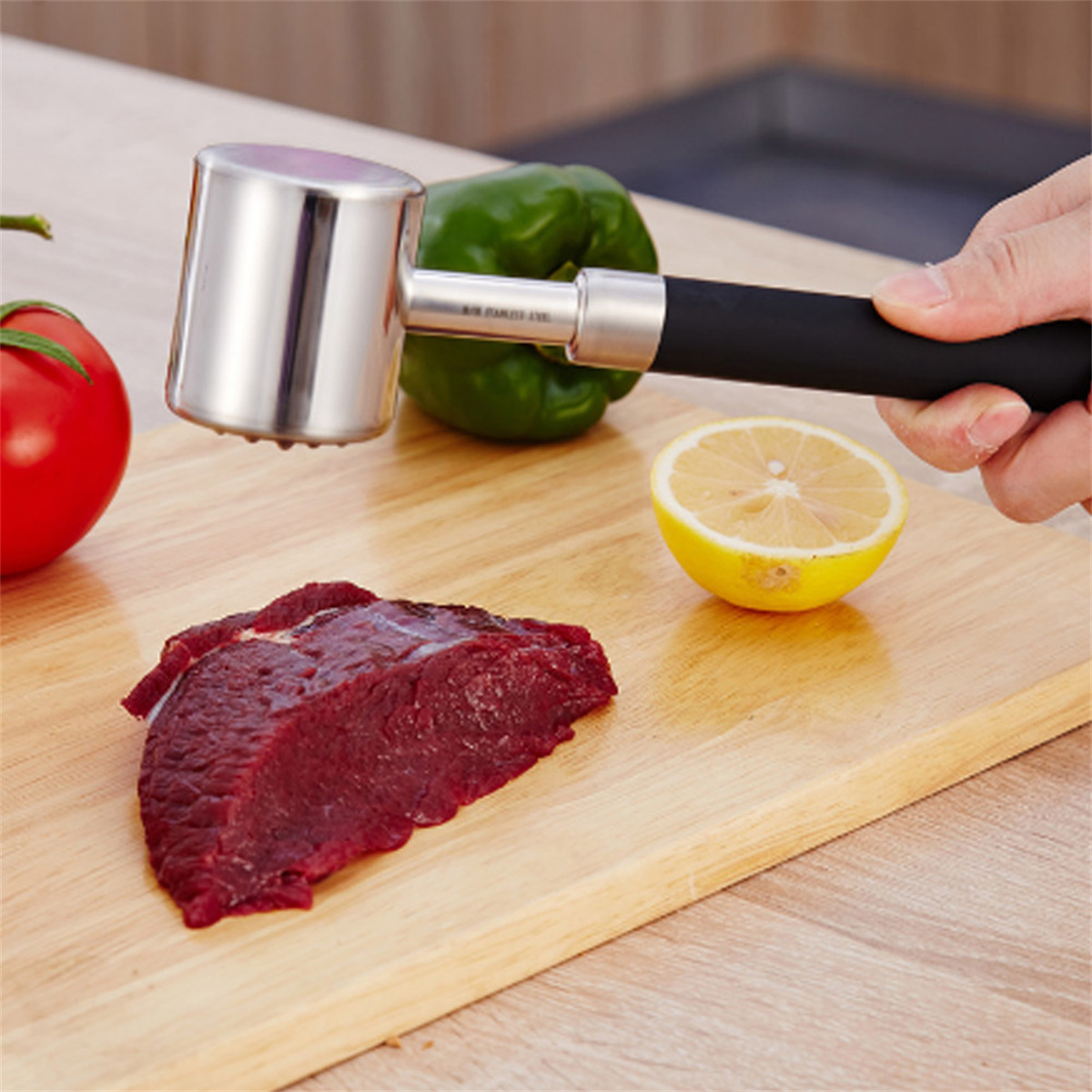 Ein Fleischklopfer auf einem Holzbrett. Eine Hand hält den Klopfer über einem Stück Fleisch. Gemüse in der Nähe.