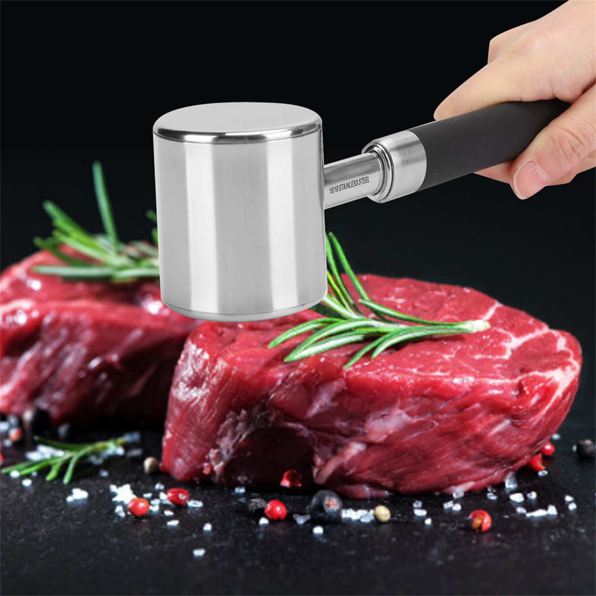Ein Fleischklopfer aus Edelstahl und zwei rohe Steaks mit Gewürzen.