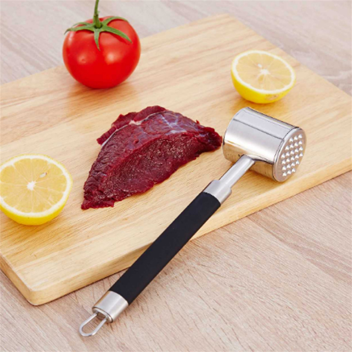 Holzschneidebrett mit rohem Fleisch, Zitronenhälften und Fleischklopfer. Alles auf Holzoberfläche.