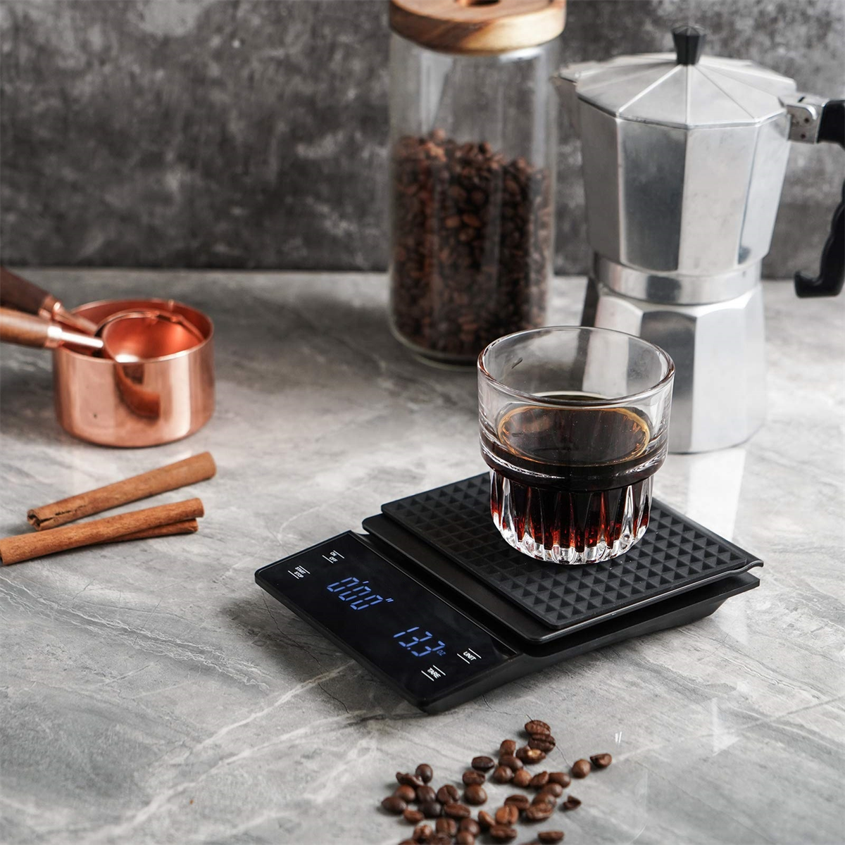Eine Kaffee-Waage mit einem Glas Kaffee, Kaffeebohnen und Messwerkzeugen. Ein digitales Display zeigt das Gewicht an.