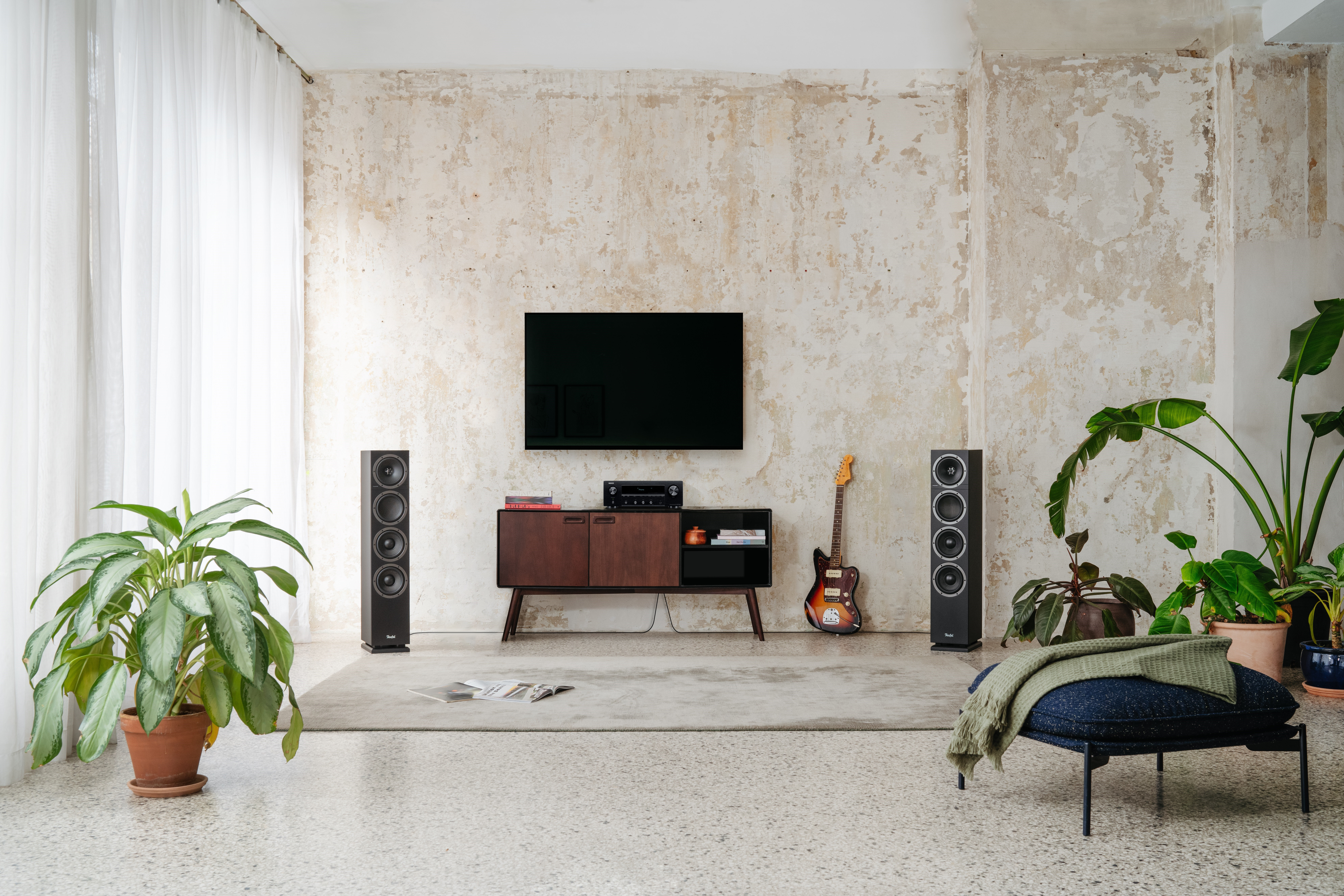 Ein Wohnzimmer mit Sofa, Lautsprechern, Fernseher und Pflanzen, das eine moderne, komfortable Atmosphäre schafft.