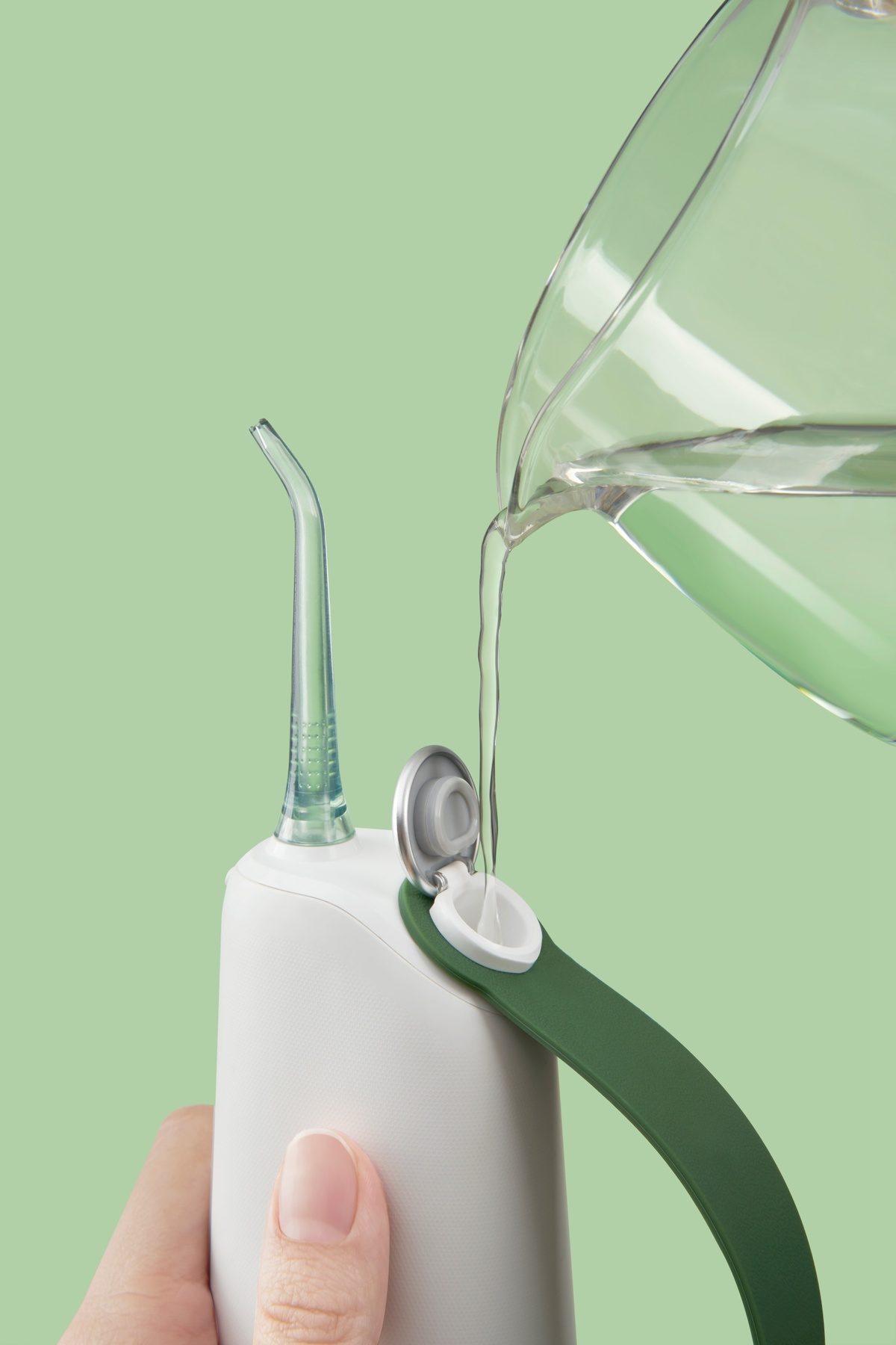 Hand gießt Wasser in einen weißen und grünen Wasserfloßer. Der Floßer hat einen grünen Griff.