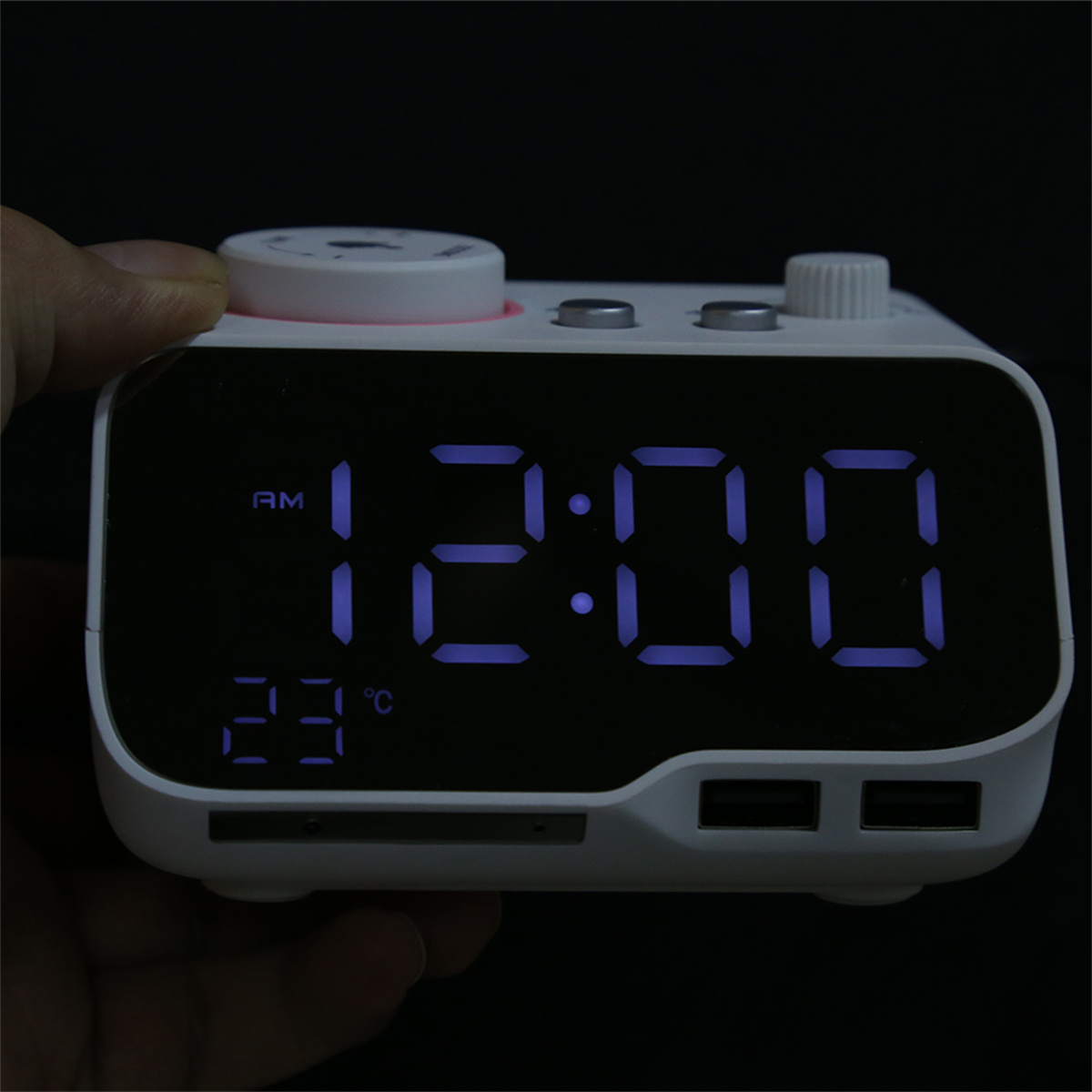 Digitaluhr mit blauen Ziffern, die 12:00 und 23°C anzeigen. Weißes Gehäuse, mit USB-Anschlüssen unten.