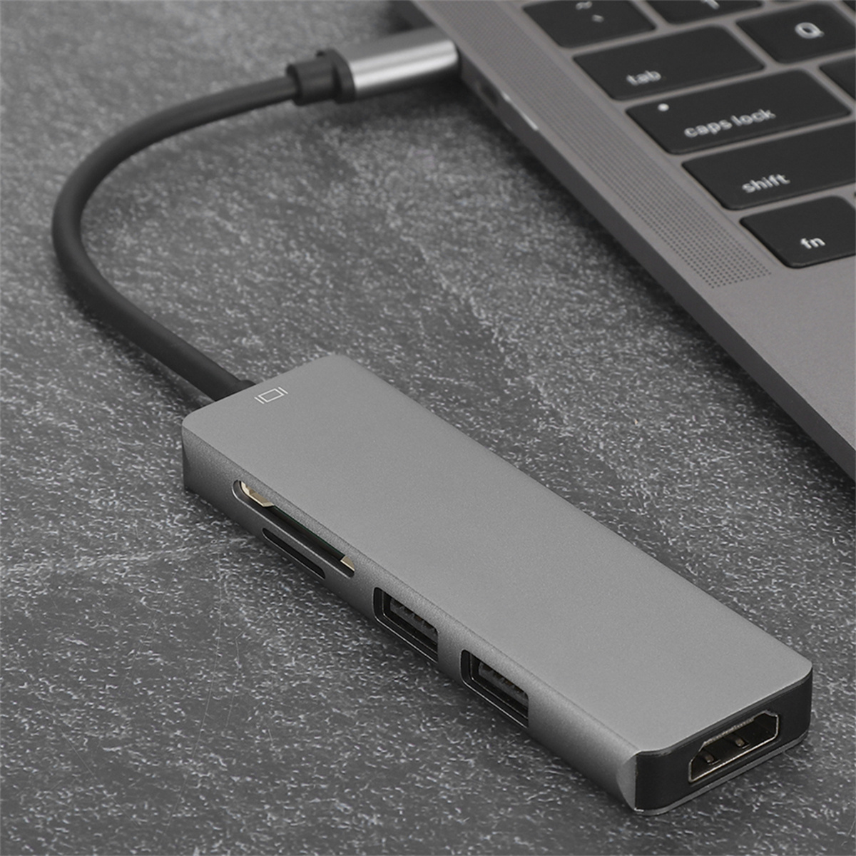 Ein grauer USB-C-Hub, der mit einem Laptop verbunden ist. Er hat mehrere Anschlüsse und ein schwarzes Kabel.
