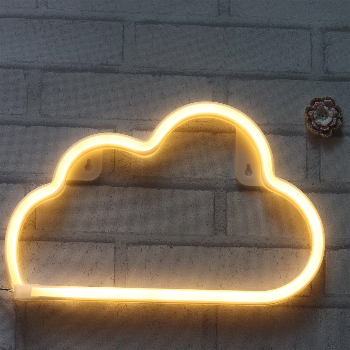 Wolkenförmige Neonleuchte, gelb leuchtend, an Backsteinmauer, Blume in der Nähe.