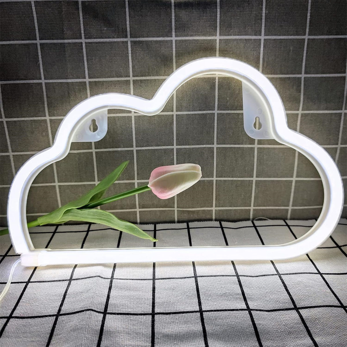 Ein weißes, wolkenförmiges Neonlicht mit einer rosa Tulpe vor kariertem Hintergrund.
