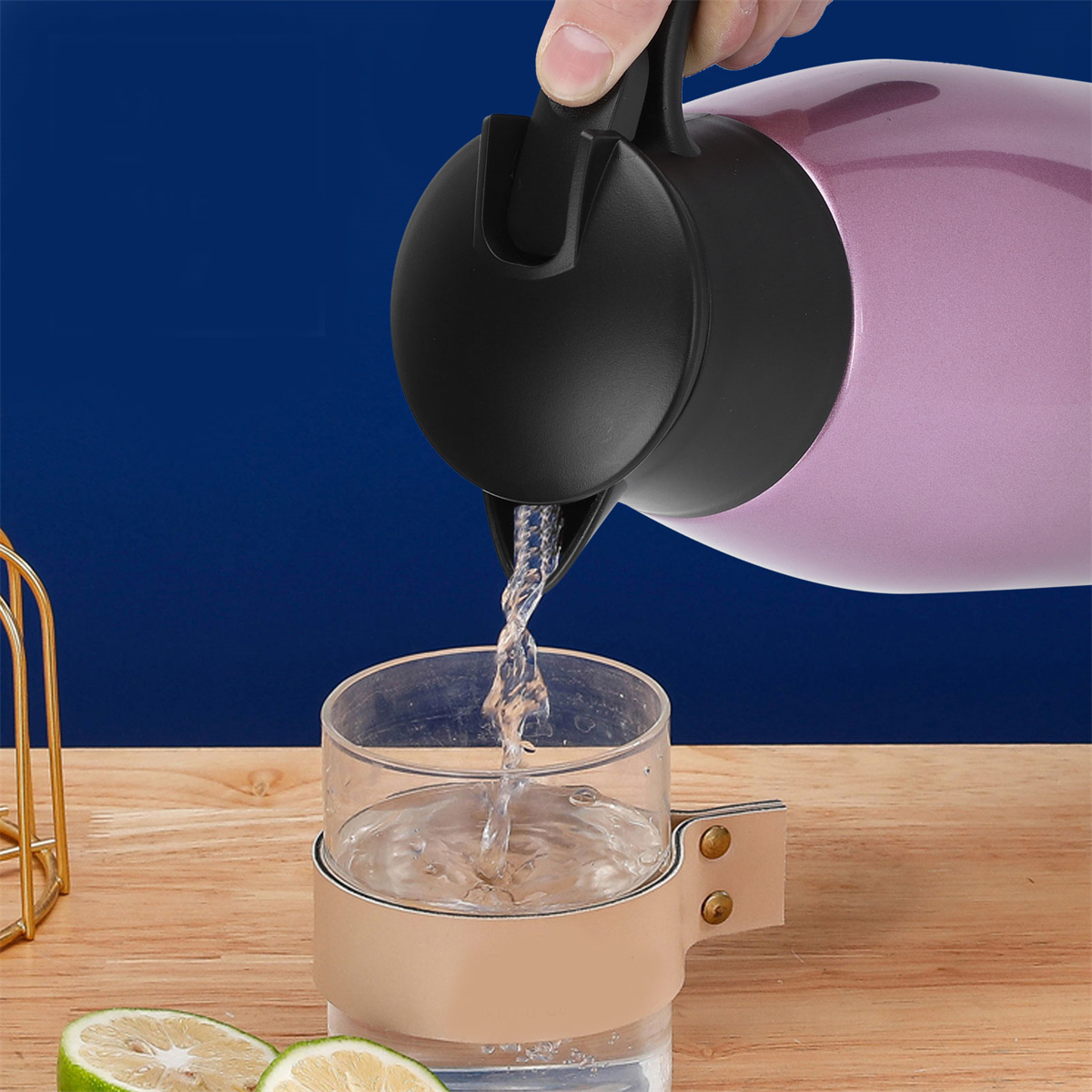Eine Hand gießt Wasser aus einer rosa Thermoskanne in ein Glas mit beigem Halter. Blauer Hintergrund.