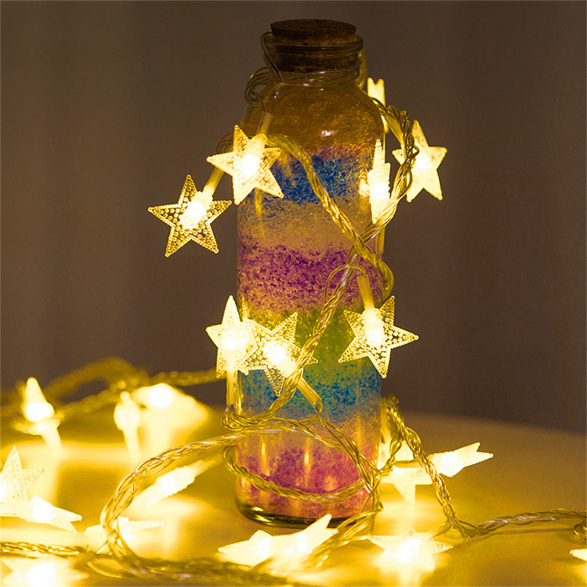 Eine Glasflasche mit farbigem Sand, umwickelt von sternförmigen, gelb leuchtenden Lichterketten.