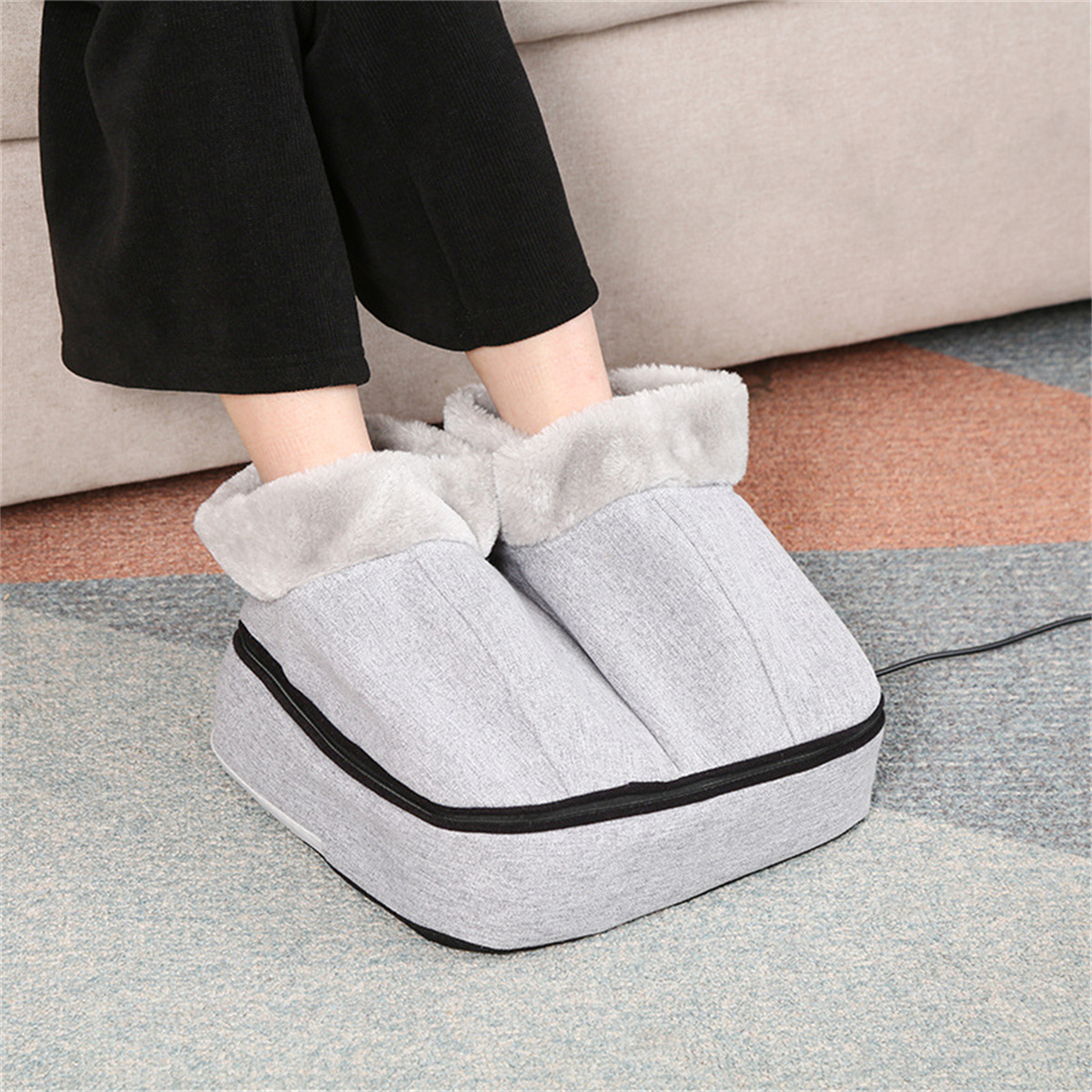 Füße in grauen, beheizten Fußmassage-Schuhen. Person sitzt auf einer Couch.