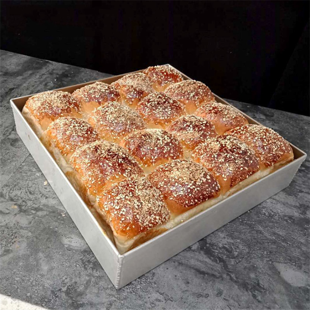 Tablett mit gebackenen Brötchen mit goldener Kruste und Sesamsamen.