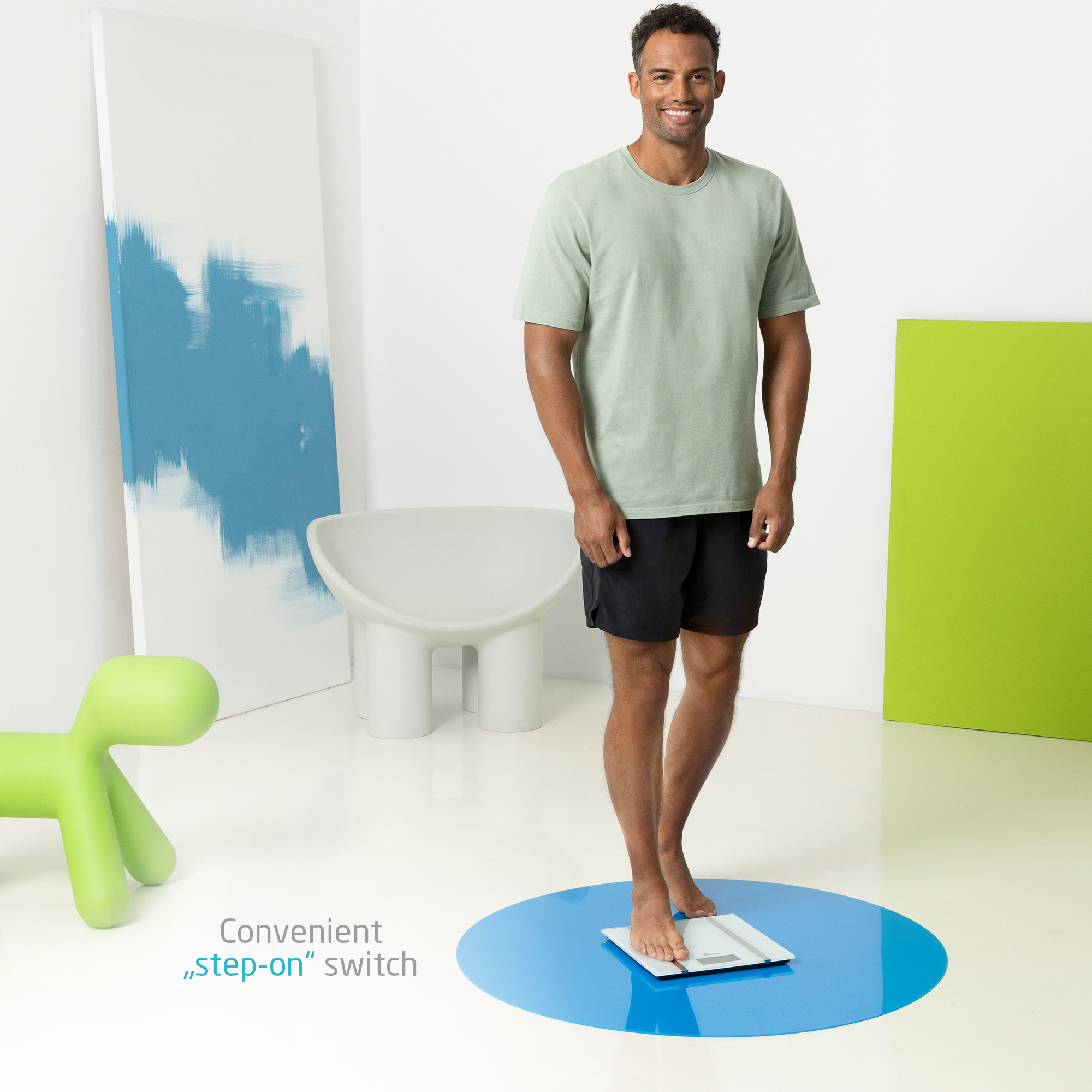 Mężczyzna stojący na wadze. Ma na sobie szorty i koszulkę. Tło przedstawia sztukę abstrakcyjną.