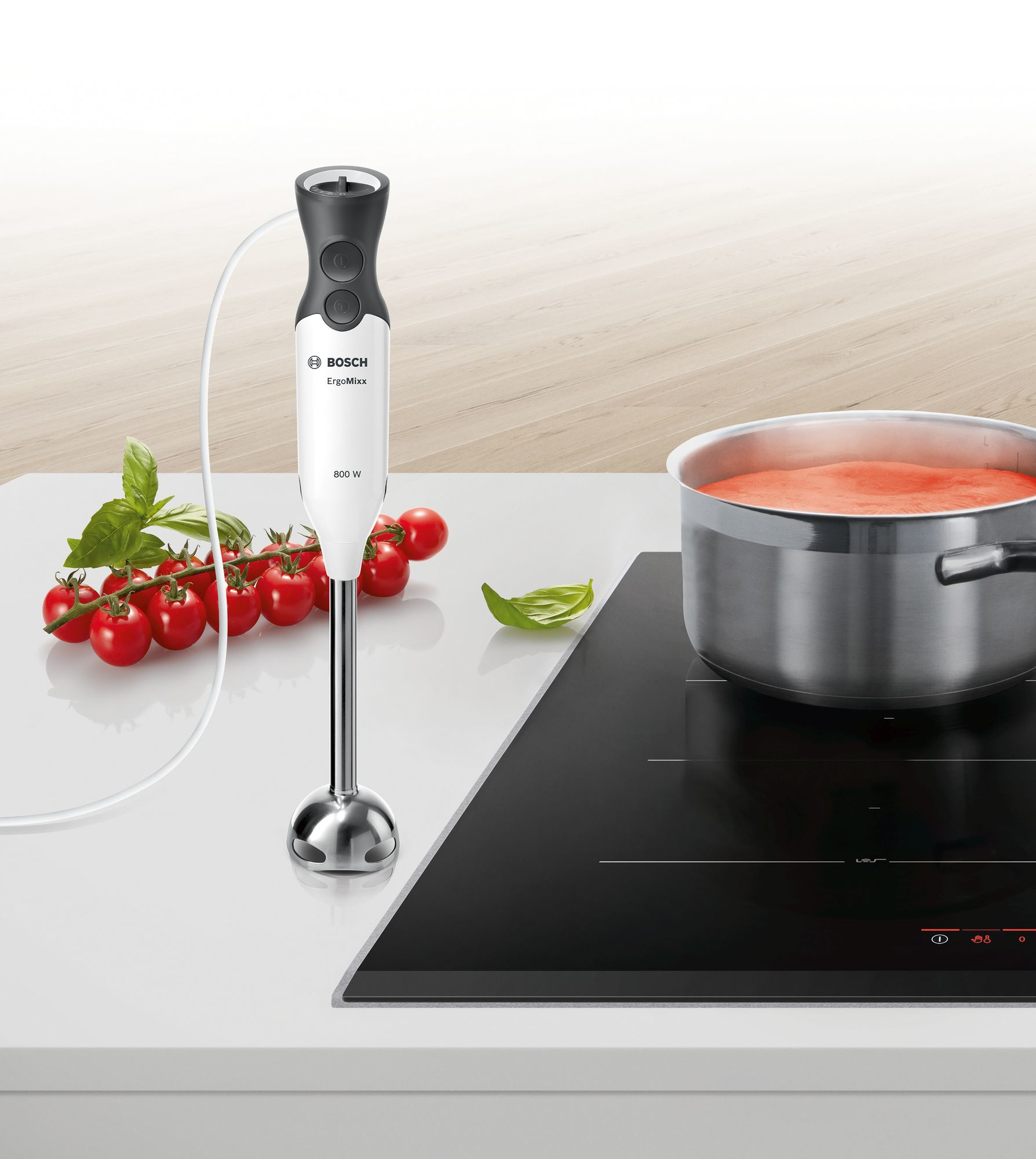 Un mixeur plongeant Bosch blanc avec de la nourriture sur un comptoir à côté d'une casserole.
