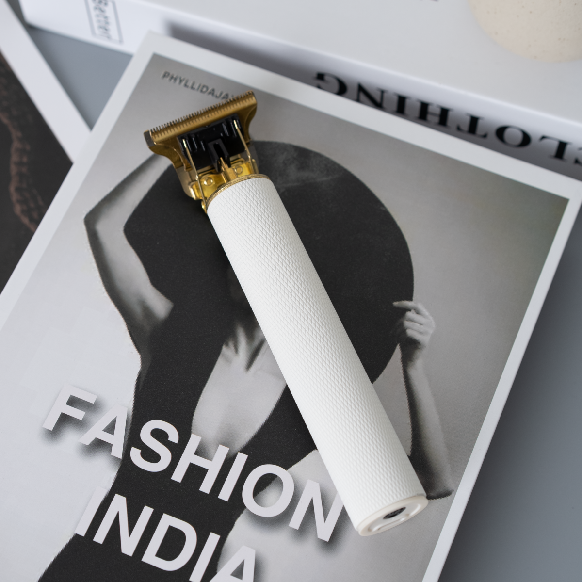 Cortapelos blanco y dorado sobre una revista, con las palabras 'FASHION INDIA' visibles.