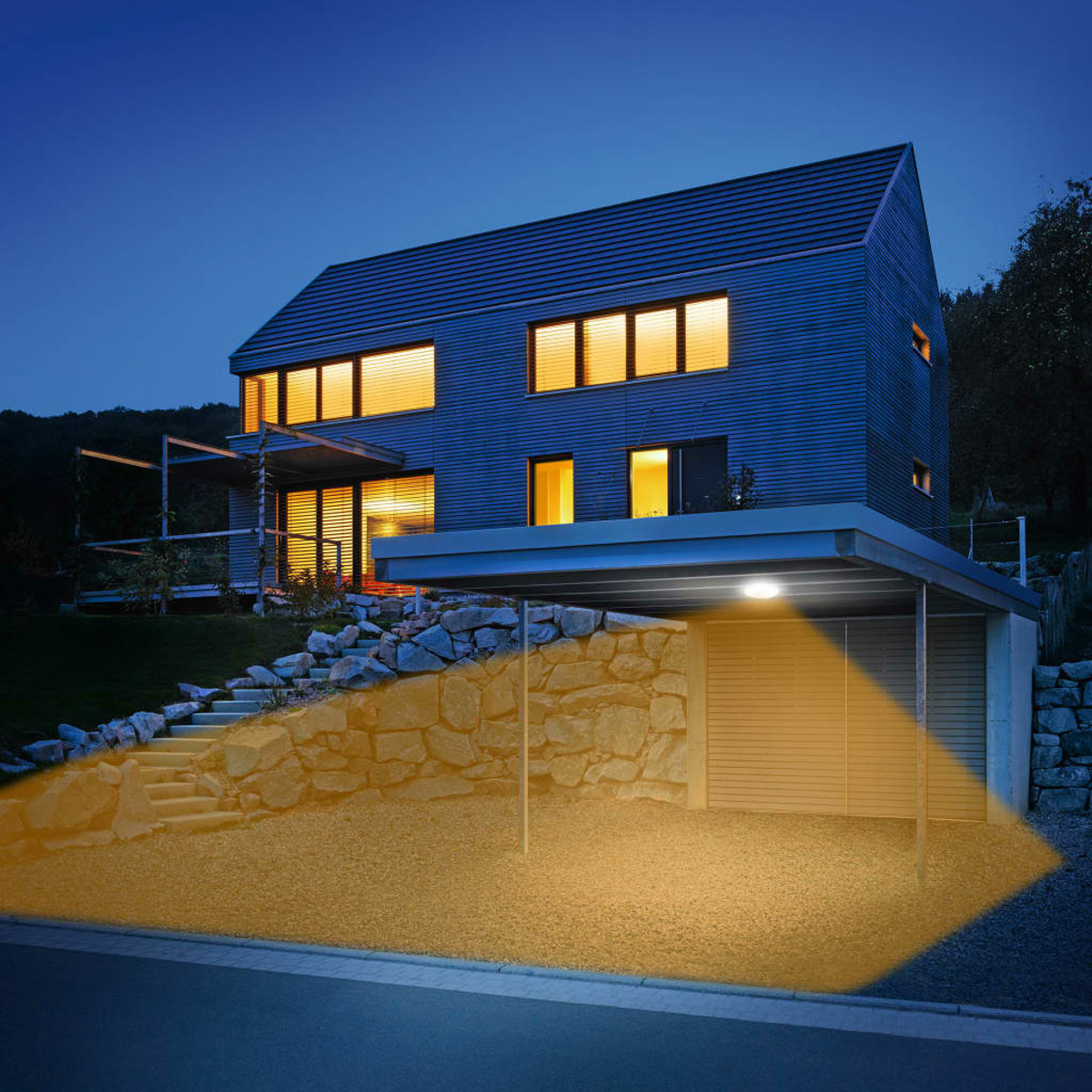 Modernes Haus mit Carport, nachts mit warmen Lichtern beleuchtet.