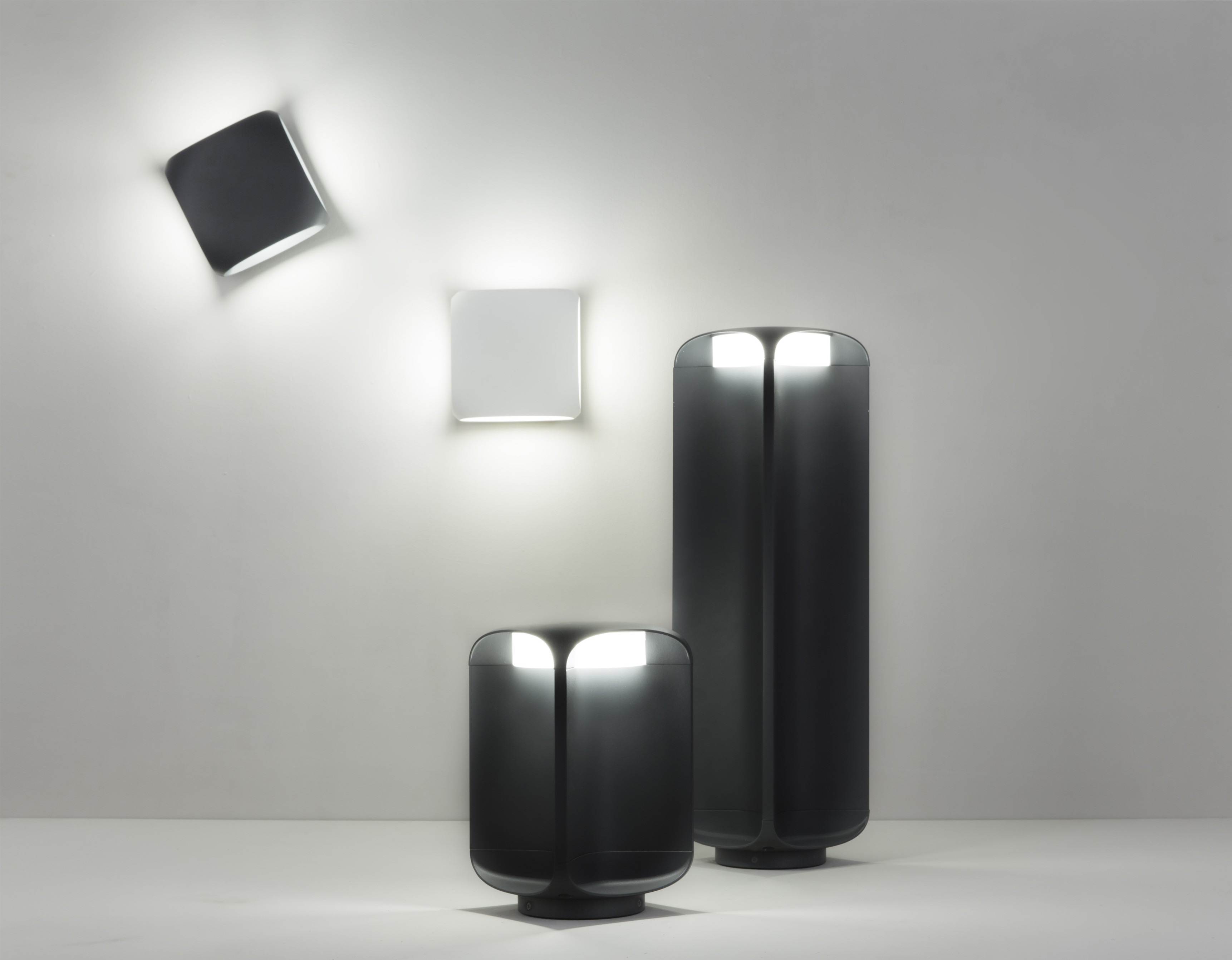 Diverse lampade, inclusi modelli a parete e da terra, con design moderno e parete bianca.