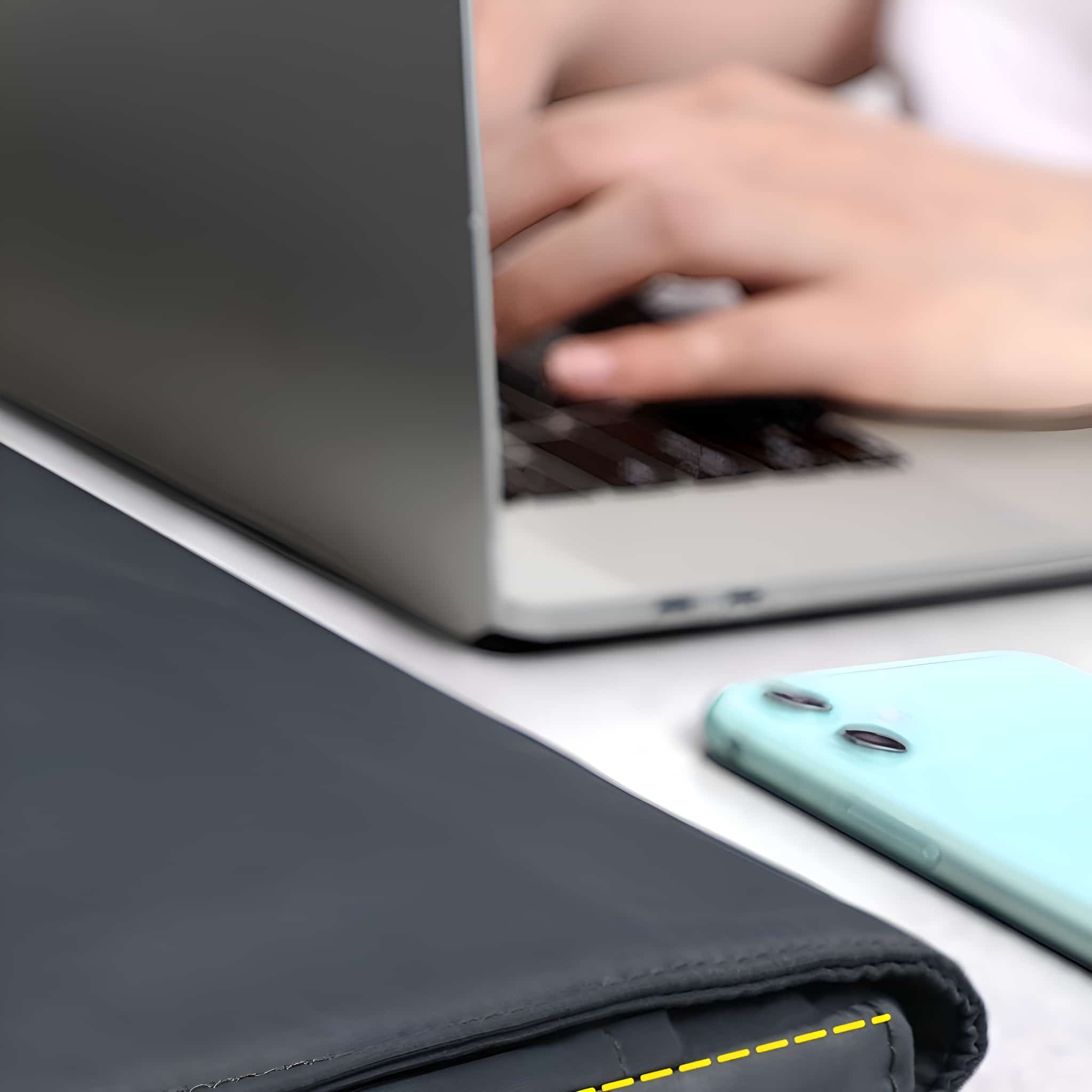 Ein Laptop, ein Telefon und ein Dokumentenhalter auf einem weißen Schreibtisch, mit einer Person, die tippt.