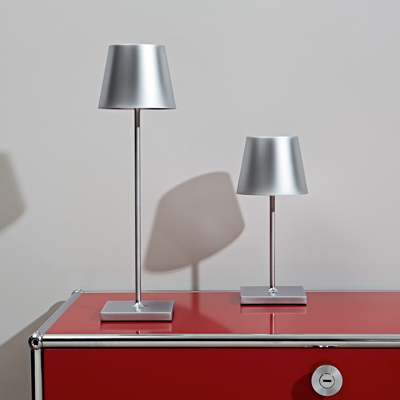 Deux lampes de table argentées avec un meuble rouge. Design minimaliste et lignes épurées.