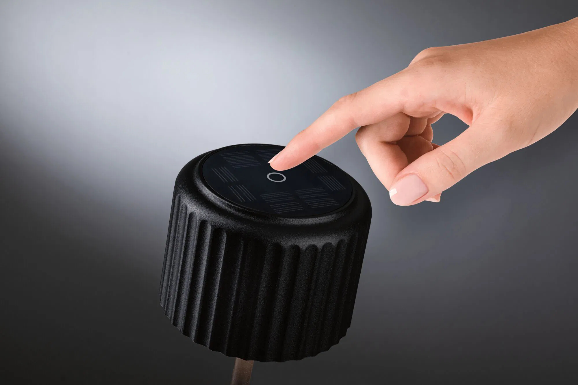 Ręka naciskająca przycisk na czarnym, teksturowanym, cylindrycznym urządzeniu.