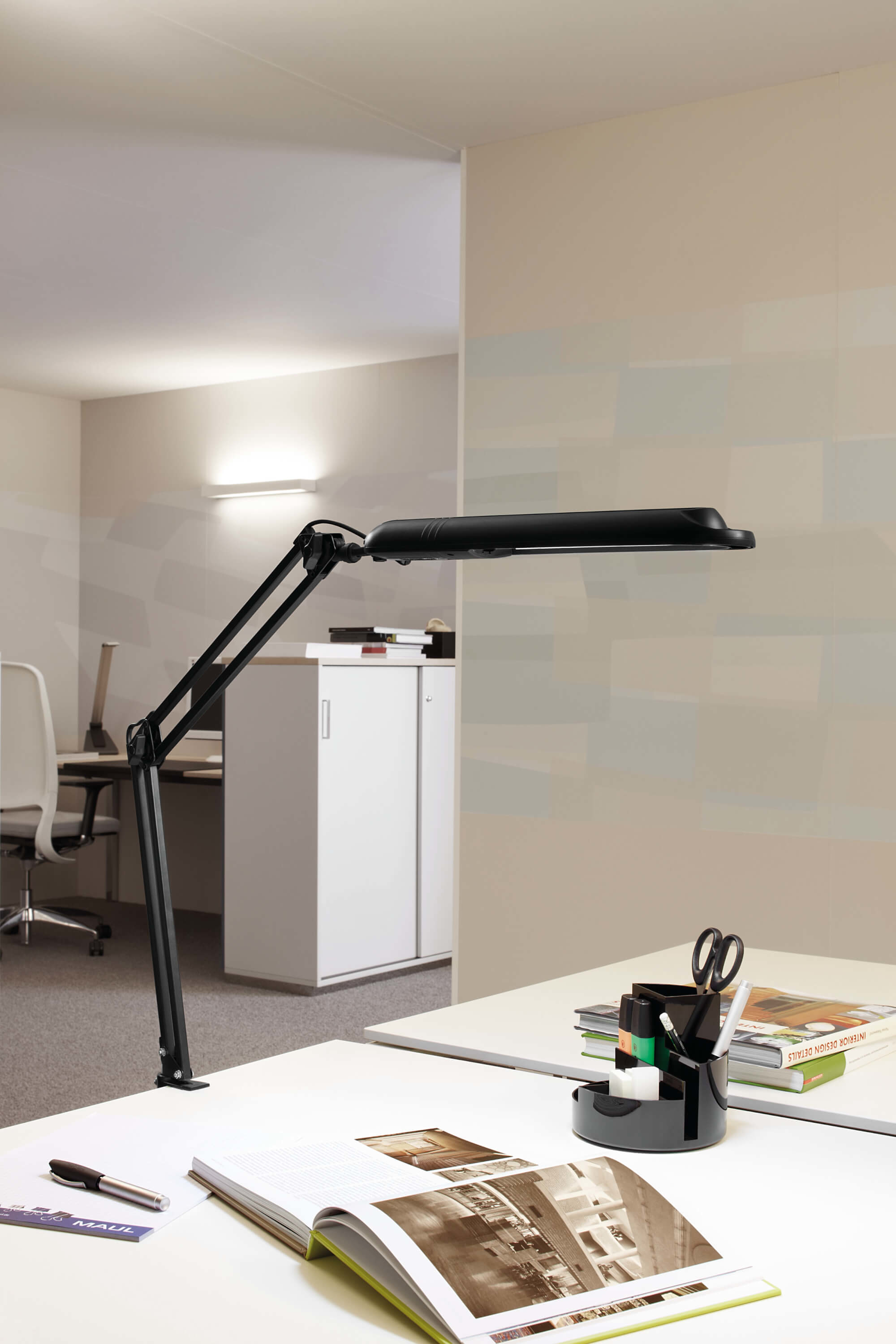 Schwarze Schreibtischlampe mit langem Arm und ein weißer Schreibtisch im Vordergrund.