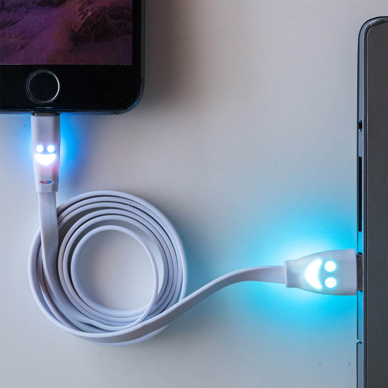 Cable de carga blanco con caras sonrientes. Conecta un teléfono y un portátil. Fondo blanco.