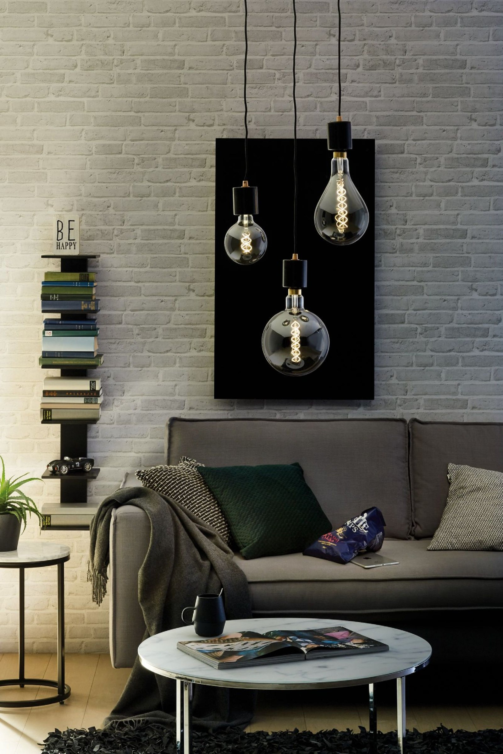 Soggiorno con tre lampadine Edison appese, un dipinto scuro e un divano grigio.