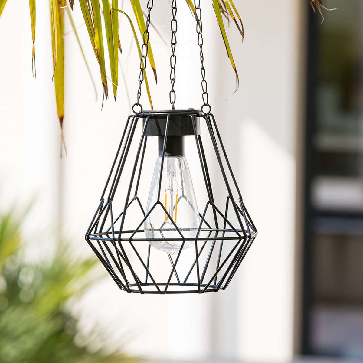 Una lampada a sospensione da esterno nera a forma di diamante con lampadina trasparente.