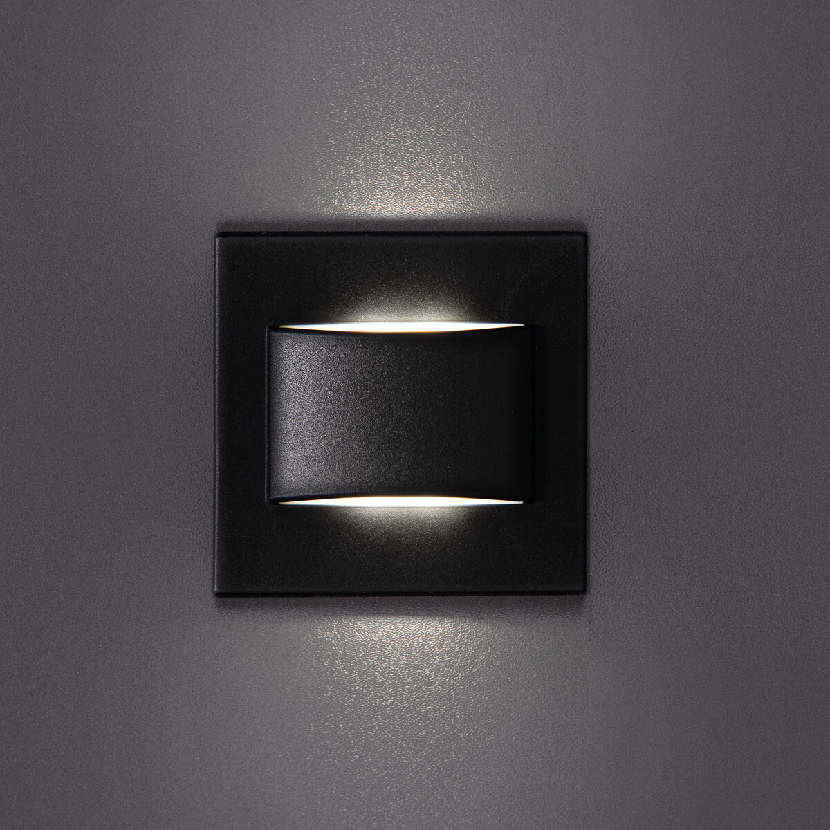 Schwarze, quadratische Wandleuchte mit geschwungener Lichtquelle. Grauer Hintergrund.