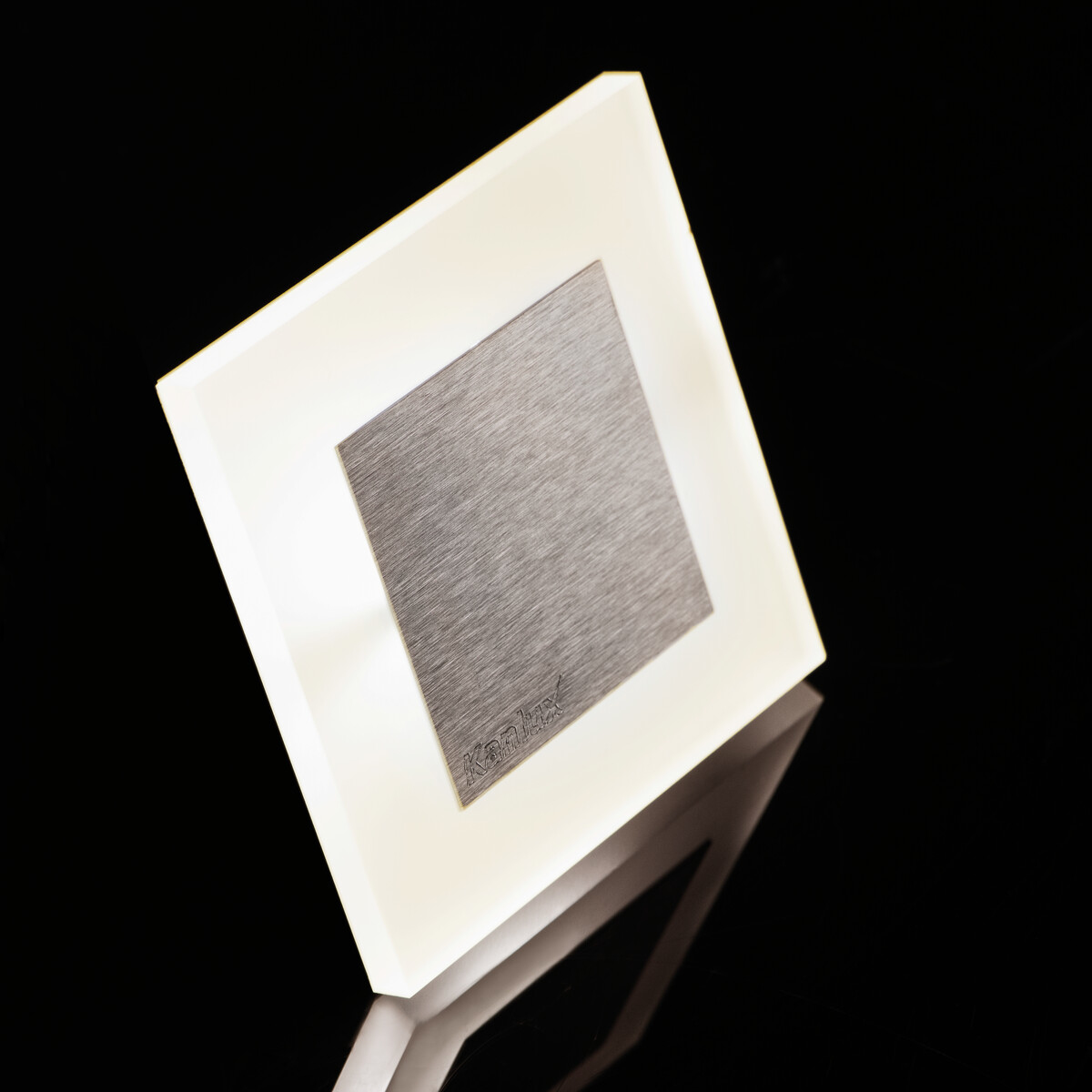 Un apparecchio di illuminazione quadrato con un centro in acciaio inossidabile e una cornice bianca. La luce è accesa.