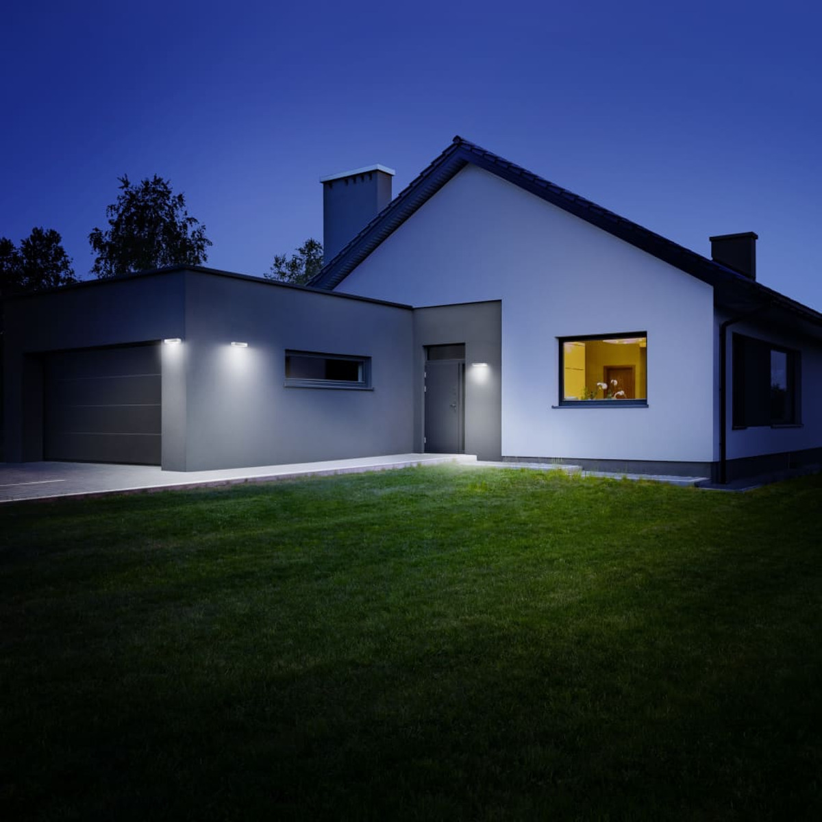 Nachtansicht eines modernen Hauses mit beleuchteten Außenleuchten und einem grünen Rasen unter einem dunkelblauen Himmel.