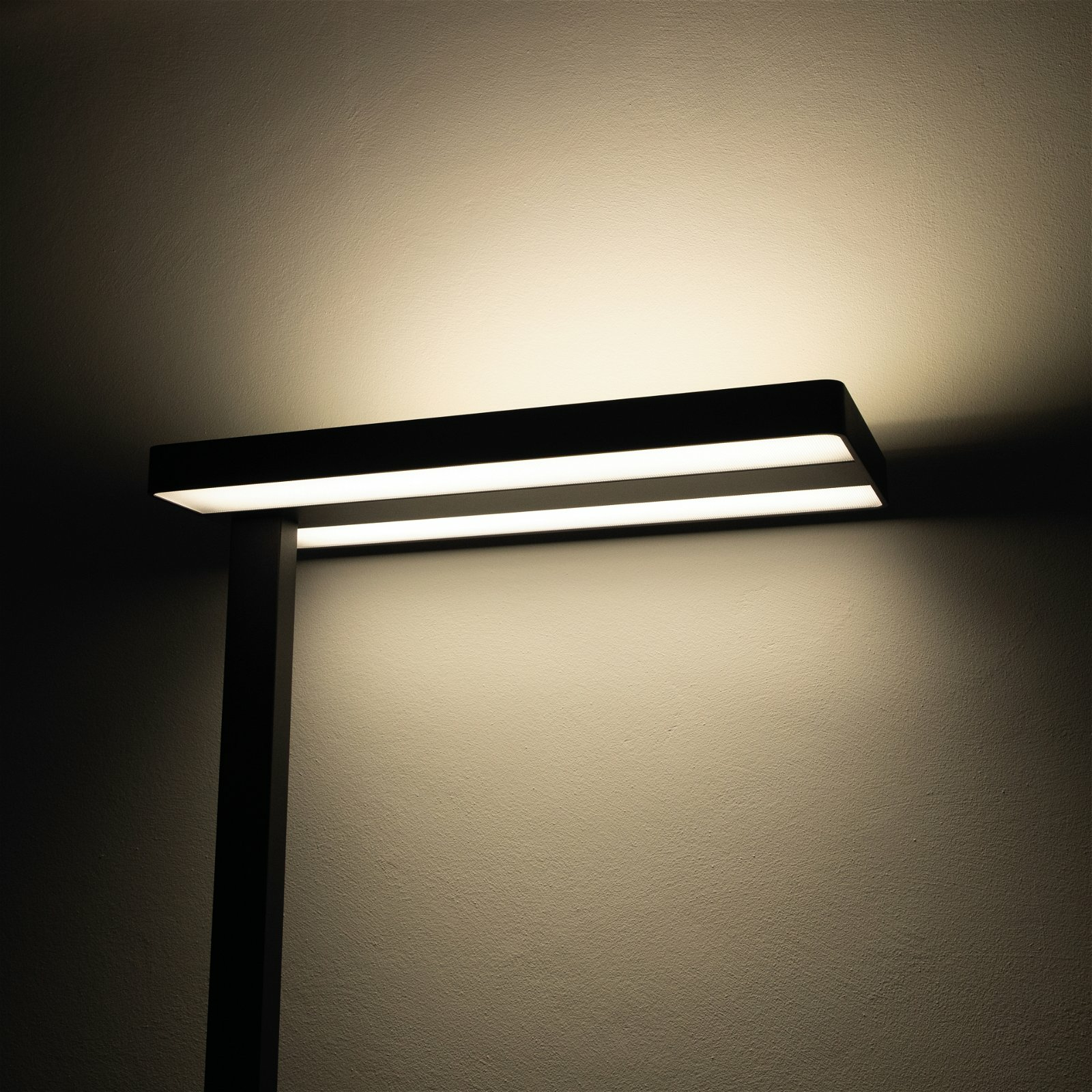 Luminaria LED rectangular negra montada en una pared, que ilumina la pared de abajo.
