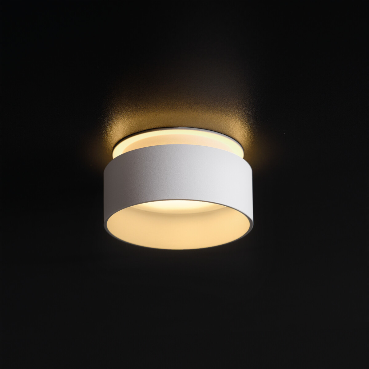 Apparecchio di illuminazione cilindrico bianco su sfondo nero, che emette luce.