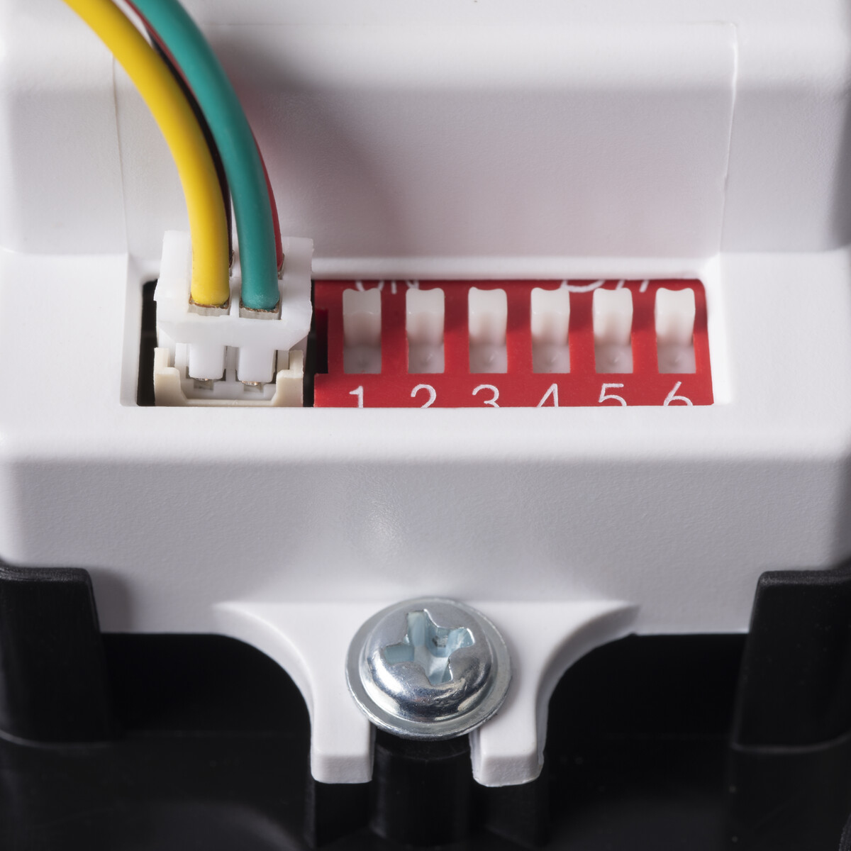 Primo piano di un componente elettrico bianco con fili colorati e un interruttore rosso.